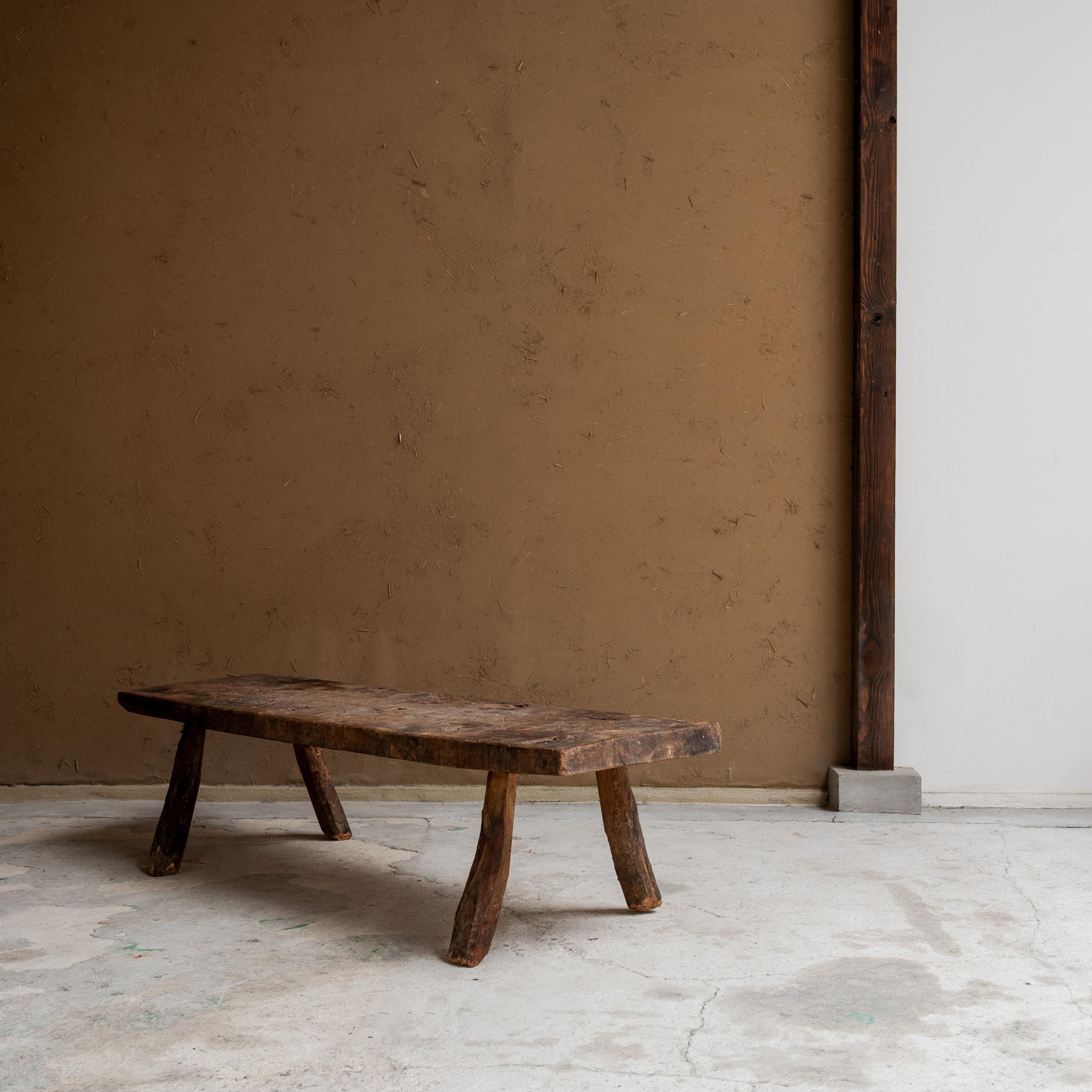 This primitive wooden bench showcases the beauty of age and material honesty. Carved from solid wood with a naturally weathered surface, the bench features irregular, hand-hewn legs and a thick, time-softened seat—each detail a testament to its