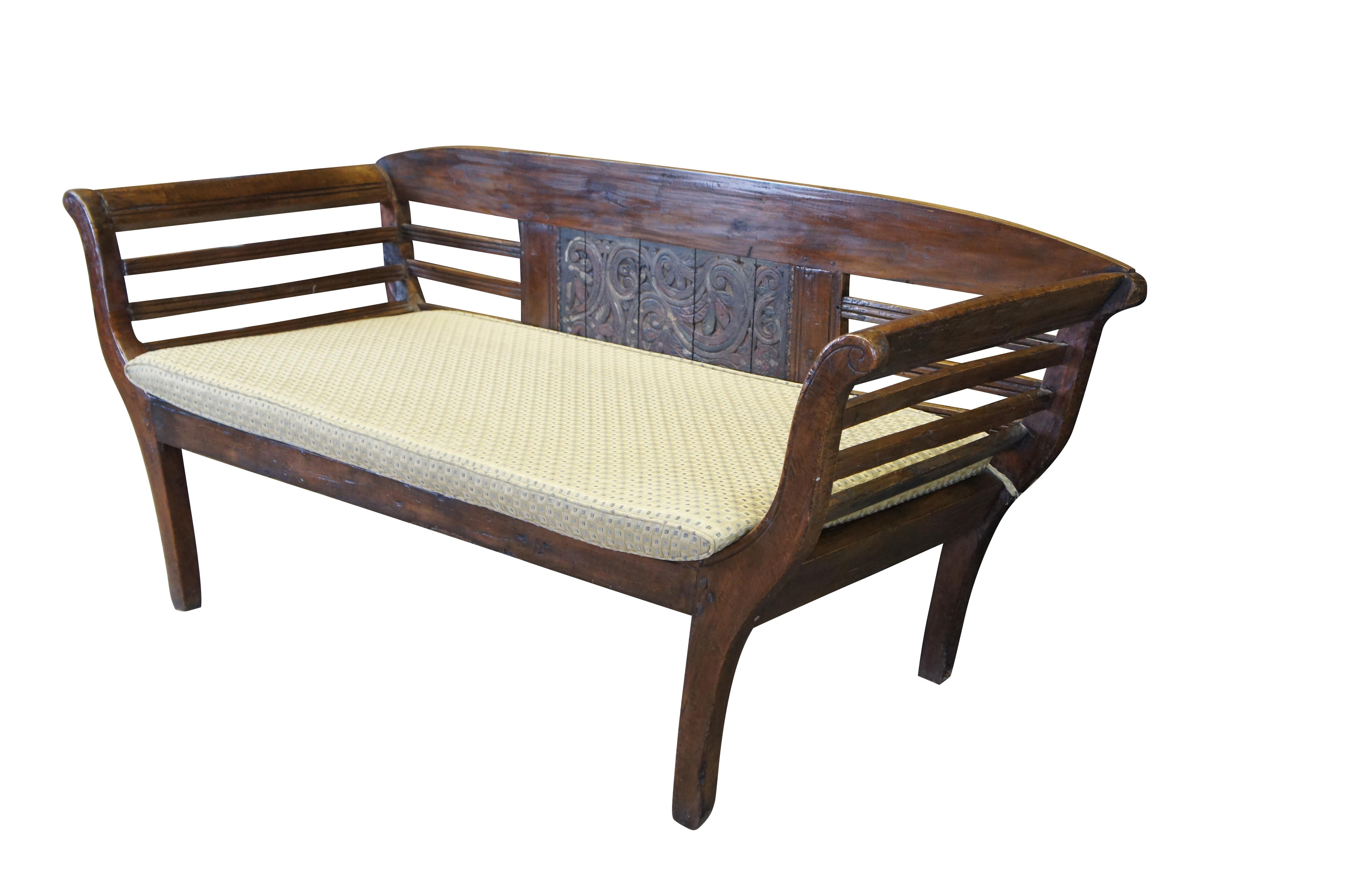 Early 20th century Indonesian / Indian country / farmhouse / colonial bench seat or settee.  Made of teak featuring ladderback design with carved floral acanthus paneled back and Jim Thompson silk upholstered cushions. 

Dimensions:
65