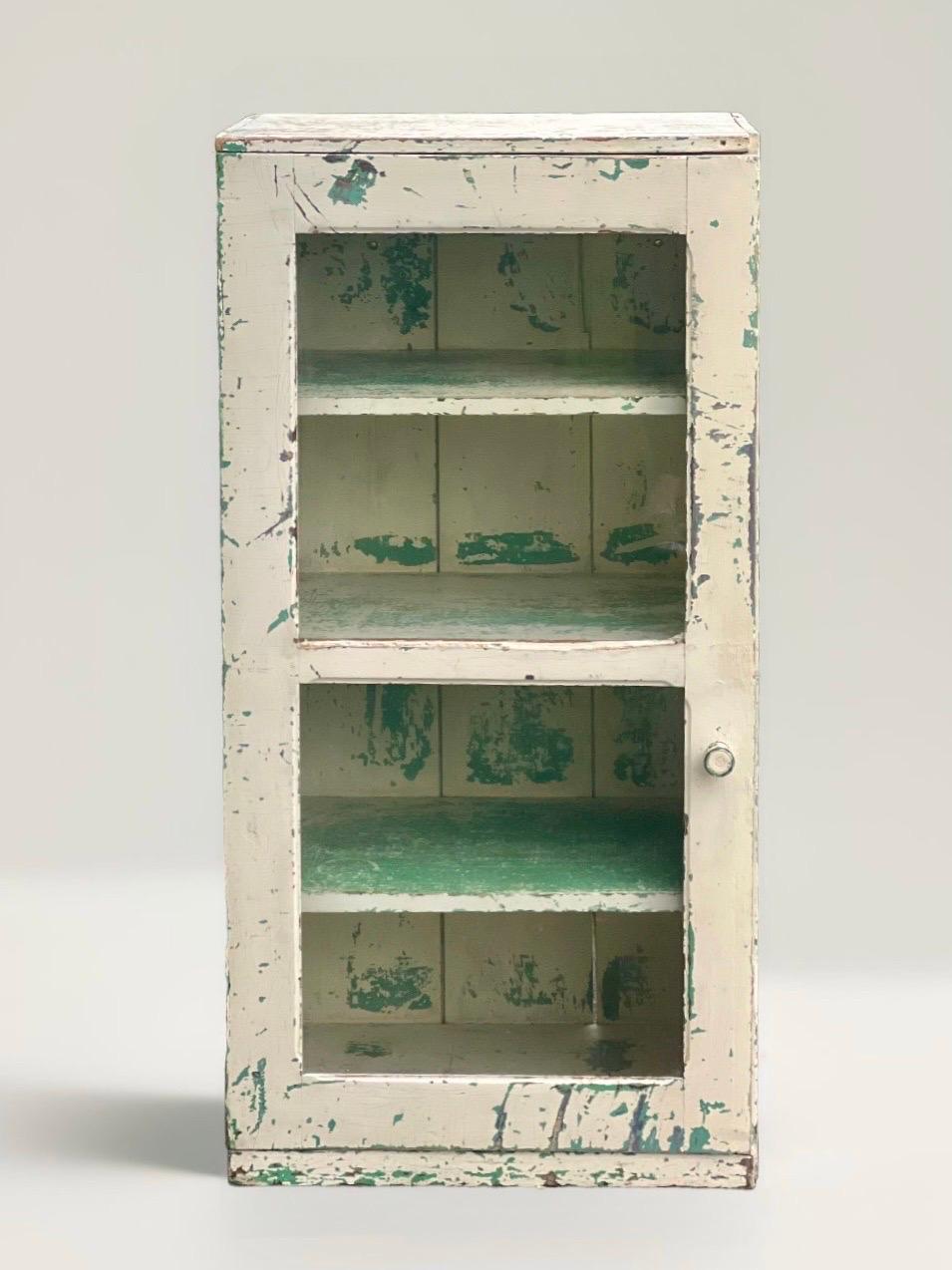 Super versatile rustic patinated single door cabinet with glass front, c. 1880-1900.

This great cabinet/cupboard has the patina of time with layers of white and green paint with three deep, fixed shelves behind a double-paned glass door. This is a
