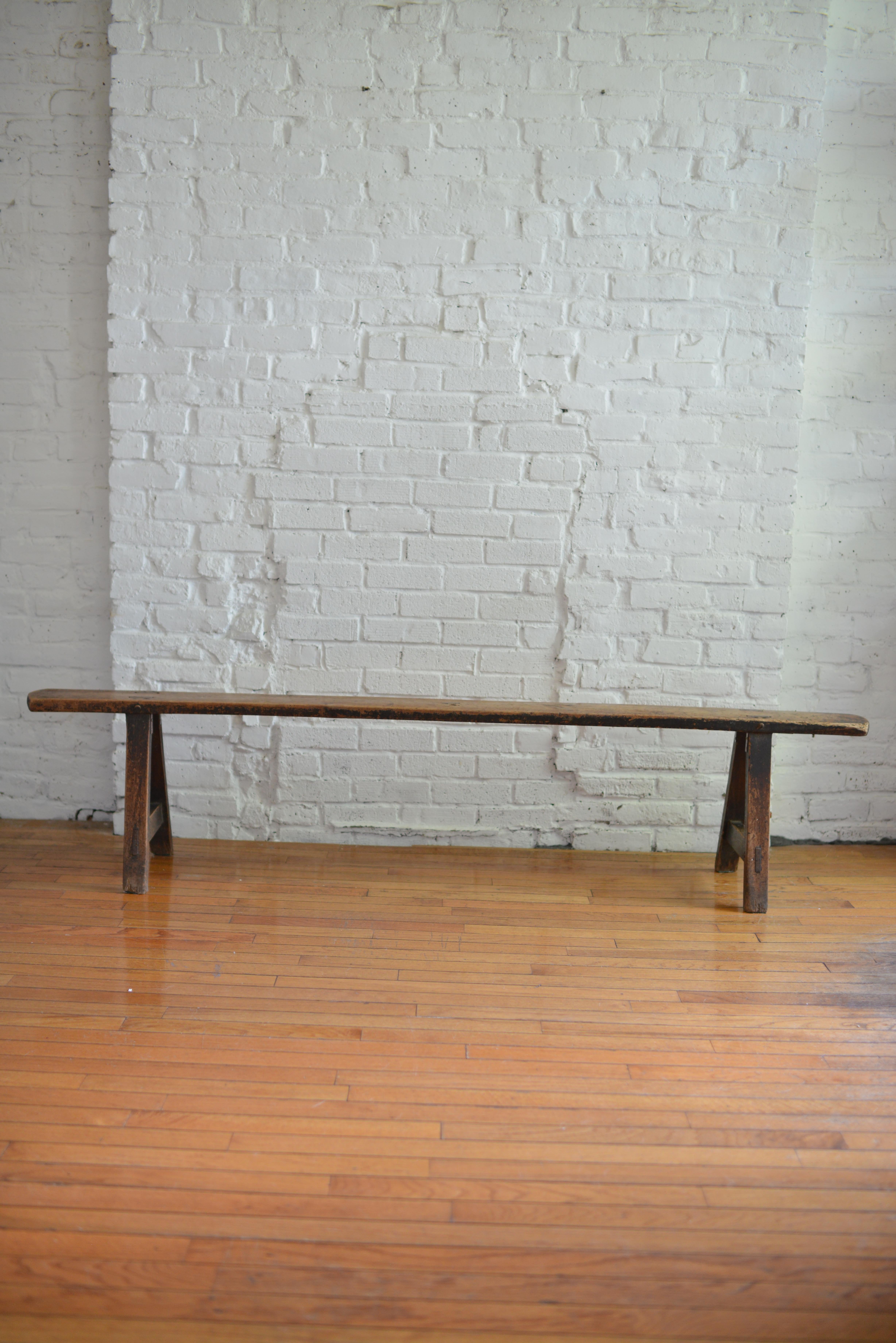 Antique primitive pine bench. This handmade bench is made of solid pine and stands on a pair of angled trestle a-frame legs with visible mortise and through tenon joinery. The six and half foot seat is built with one single rectangular board plank