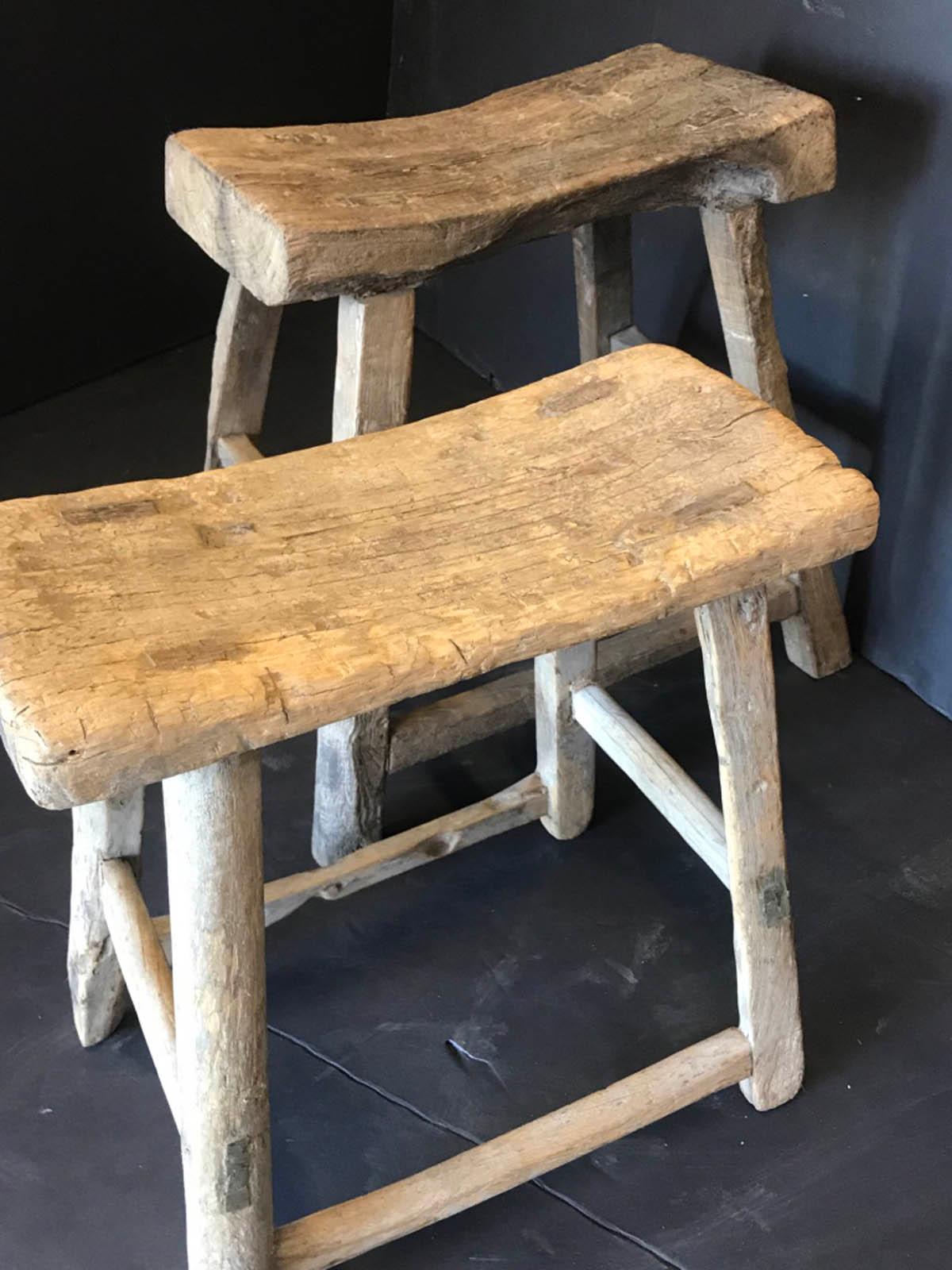 Two Primitive elm wood stools, sold separately. Mortise and tenon construction. The left in the back with darker patina has overall dimensions of 23 x 15 x 20.5 inches and the seat is 18.5 x 9.5 and about three inches thick. The right one is 17.5 x