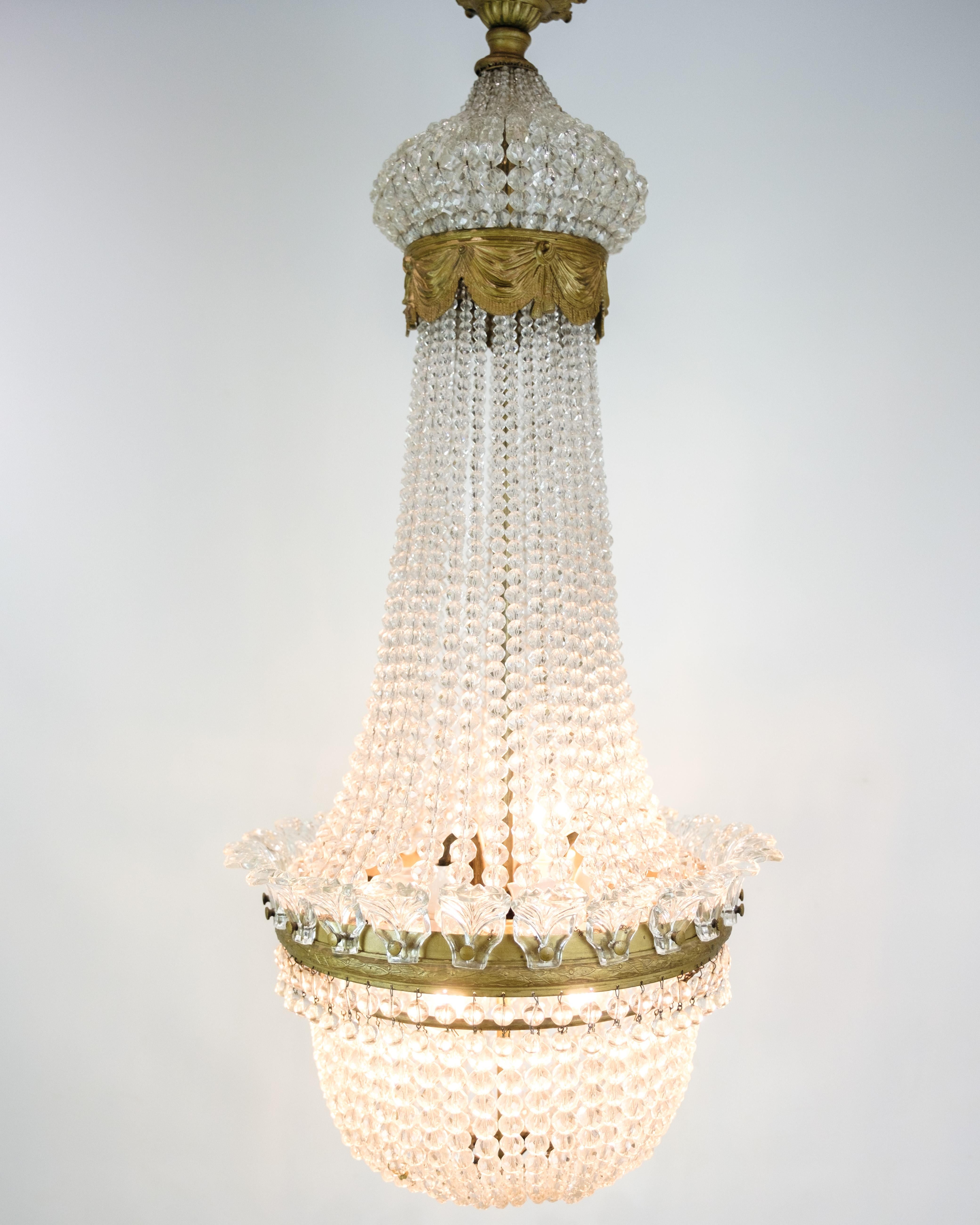 Antico lampadario a prisma del 1890, realizzato in ottone e bronzo, dorato e decorato con cristalli. Questo lampadario è un esempio della raffinata maestria dell'epoca, dove metalli preziosi e cristalli creano un'atmosfera lussuosa e senza
