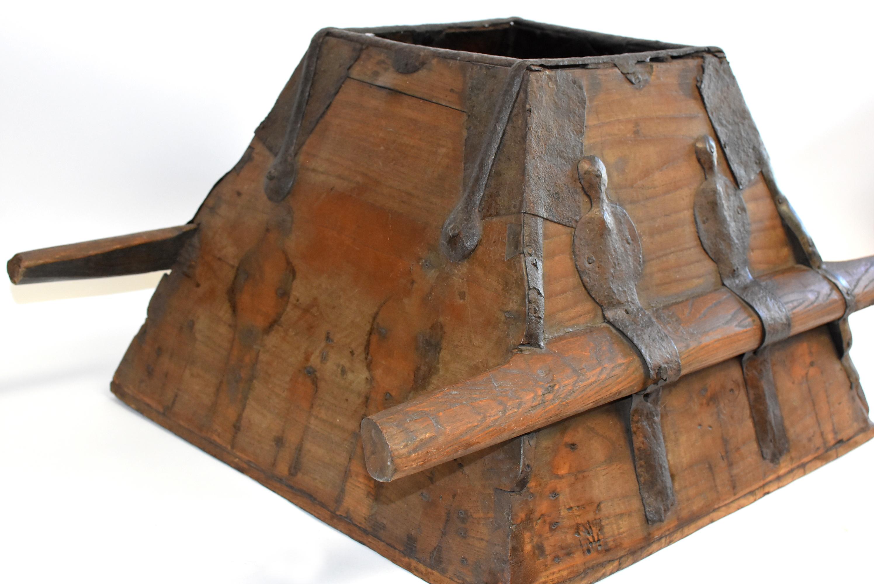 A solid wood trapezoid shaped bucket from northern China, province of Shann XI. The solid construction is reinforced by bands of hand-forged iron strips. Two solid handle bars are held securely by the same iron braces that also protect all corners.