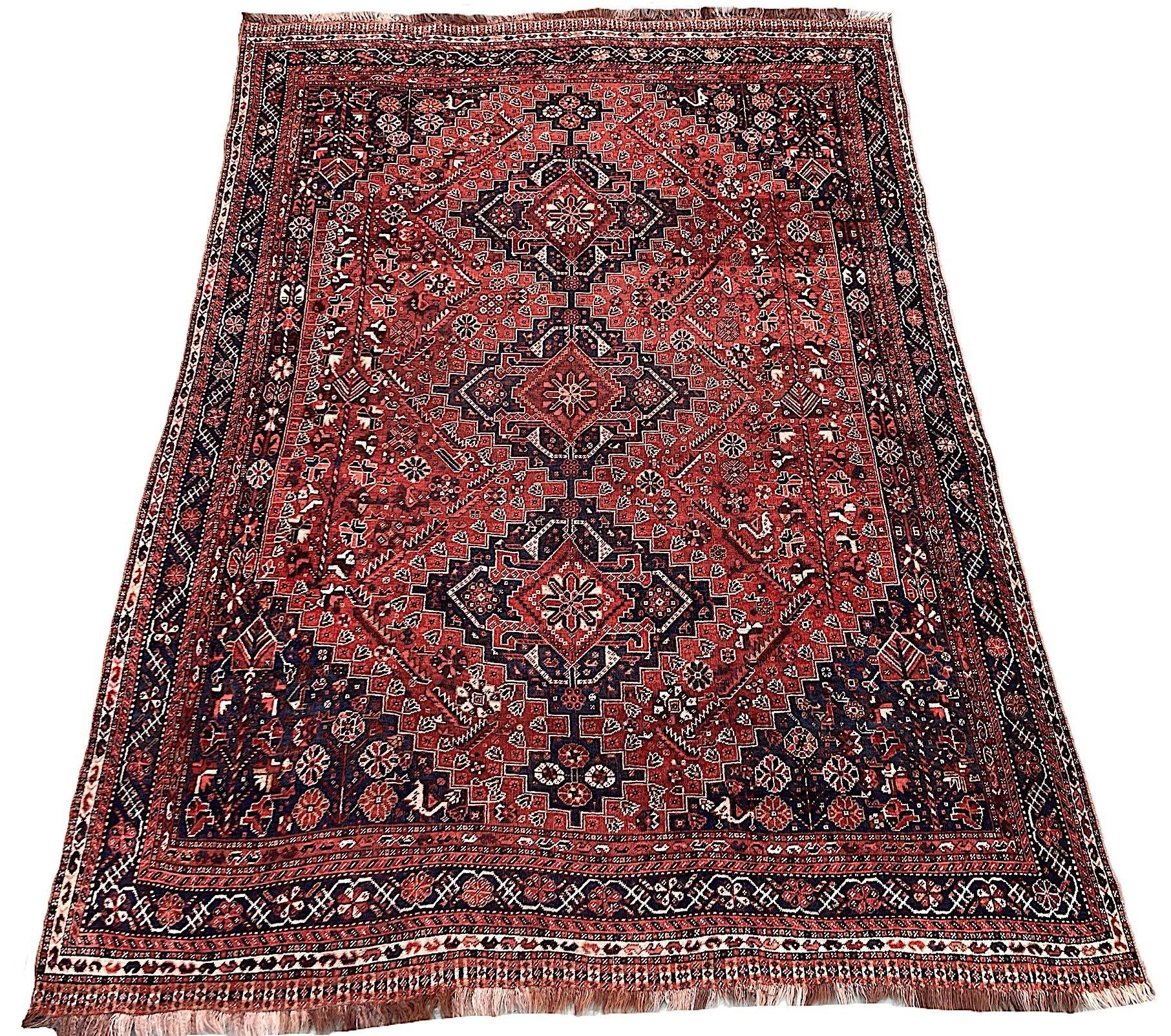 An unusually large antique Qashqai carpet, hand woven by the eponymous nomadic tribe circa 1920. The design features 3 small medallions on a terracotta field of stylised flowers and figures surrounded by an indigo border of trailing vines and