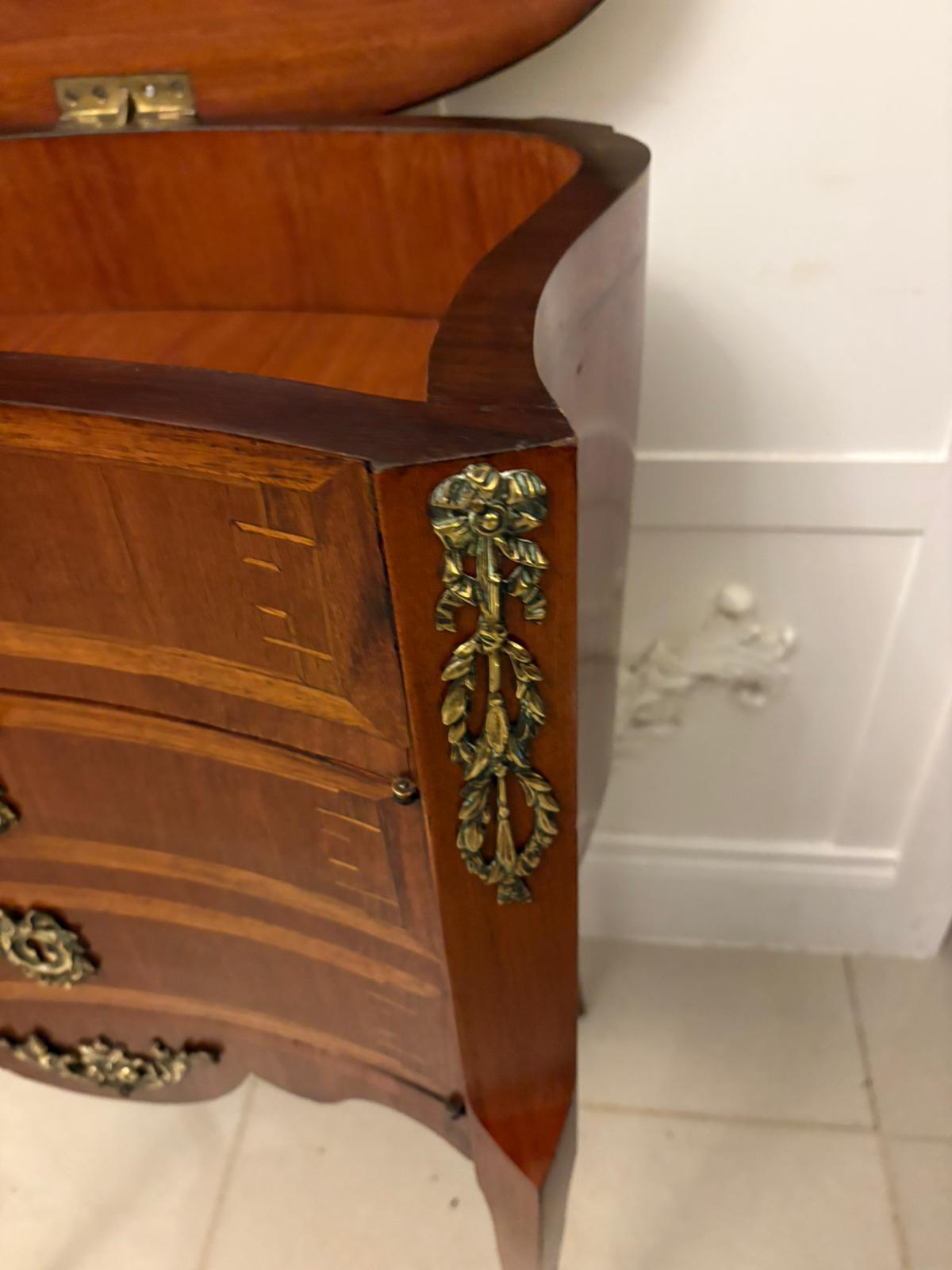 Un raffinato armadietto antico francese in stile Luigi XV splendidamente realizzato con impiallacciature di legno di re e di tulipano, con squisiti intarsi floreali e montature in bronzo dorato (ormolu).

Il piano sagomato, orlato da una galleria