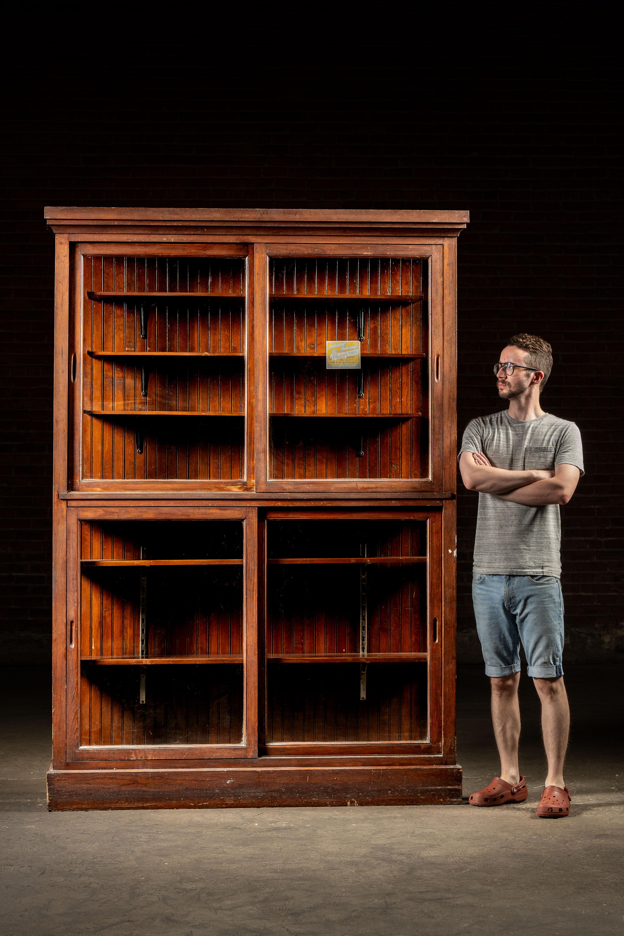 Early 20th-century oak display cabinet featuring four large sliding glass panels and a back of solid oak panels in classic quarter-sawn grain. Adjustable interior shelving is supported on original steel bracket standards, allowing flexible