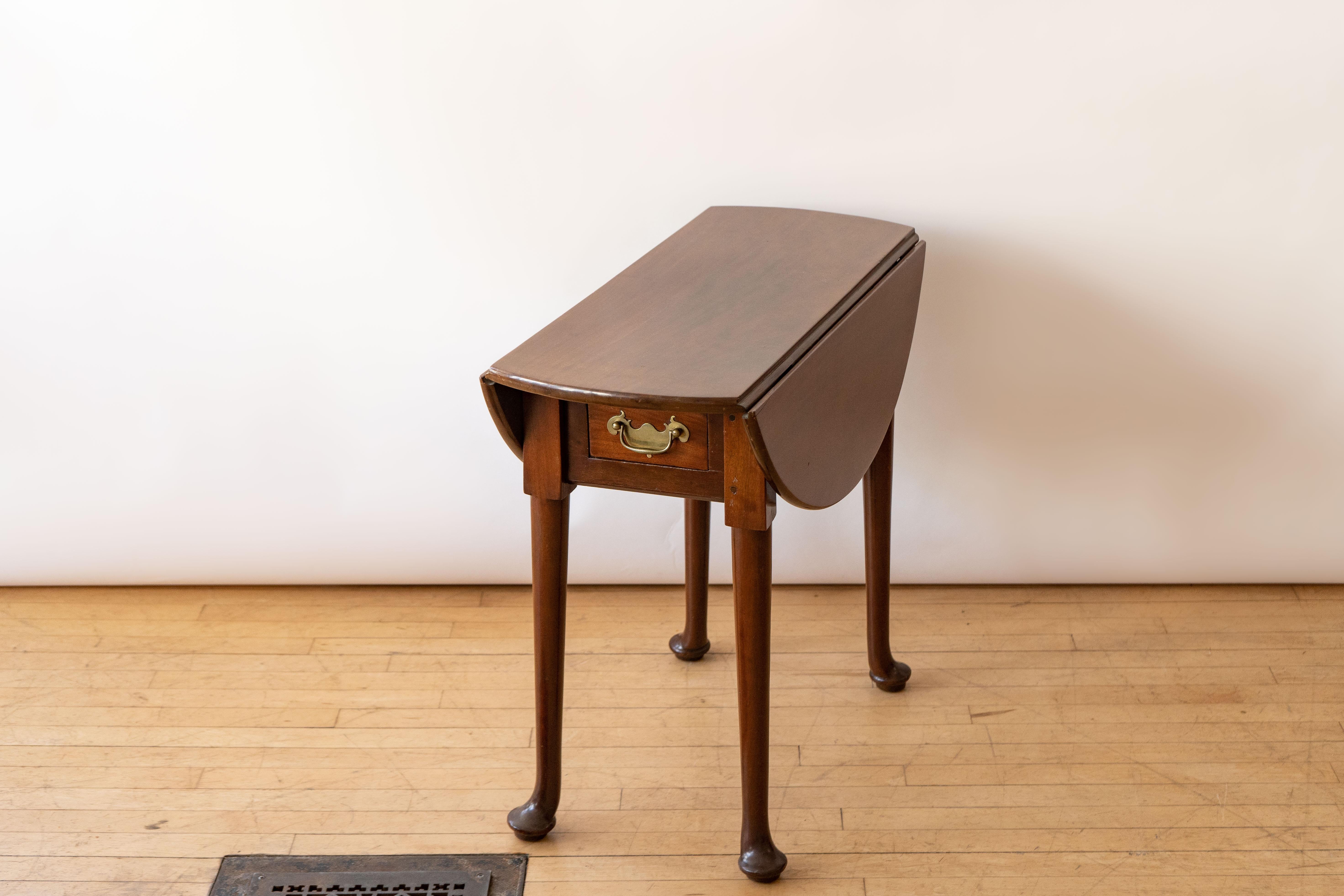 England, ca. 1750. An antique Queen Anne drop leaf breakfast table. Features solid mahogany construction with oak secondary woods and thick legs supported by rounded “duck” feet. Two small drawers with original brass pulls provide storage. Works