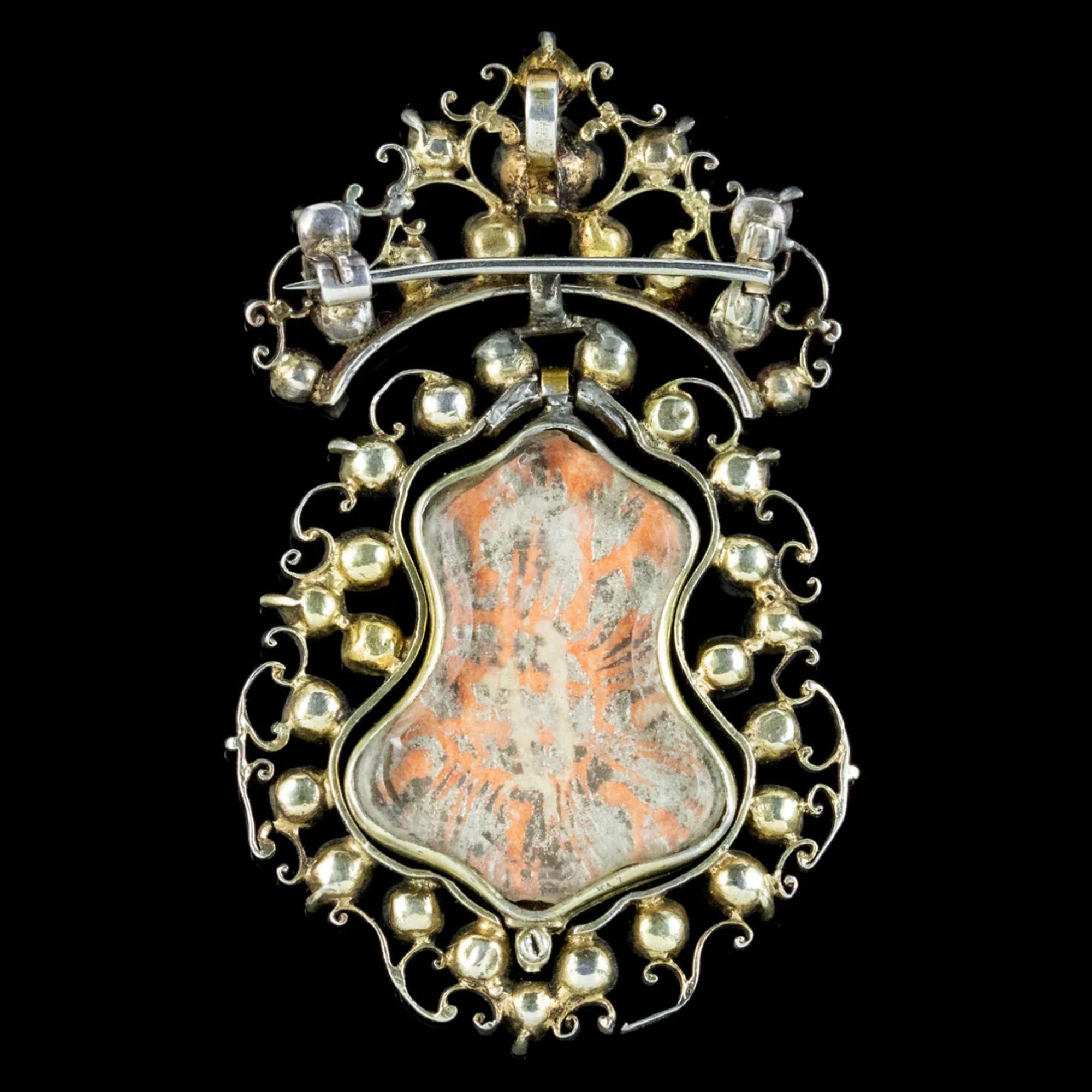 A rare Antique Queen Anne pendant/ brooch from the early 1700s decorated with an array of colourful old cut Paste stones dotted across an open worked Silver gallery with scrolling foliate metalwork.

A double-sided locket is held in the centre with