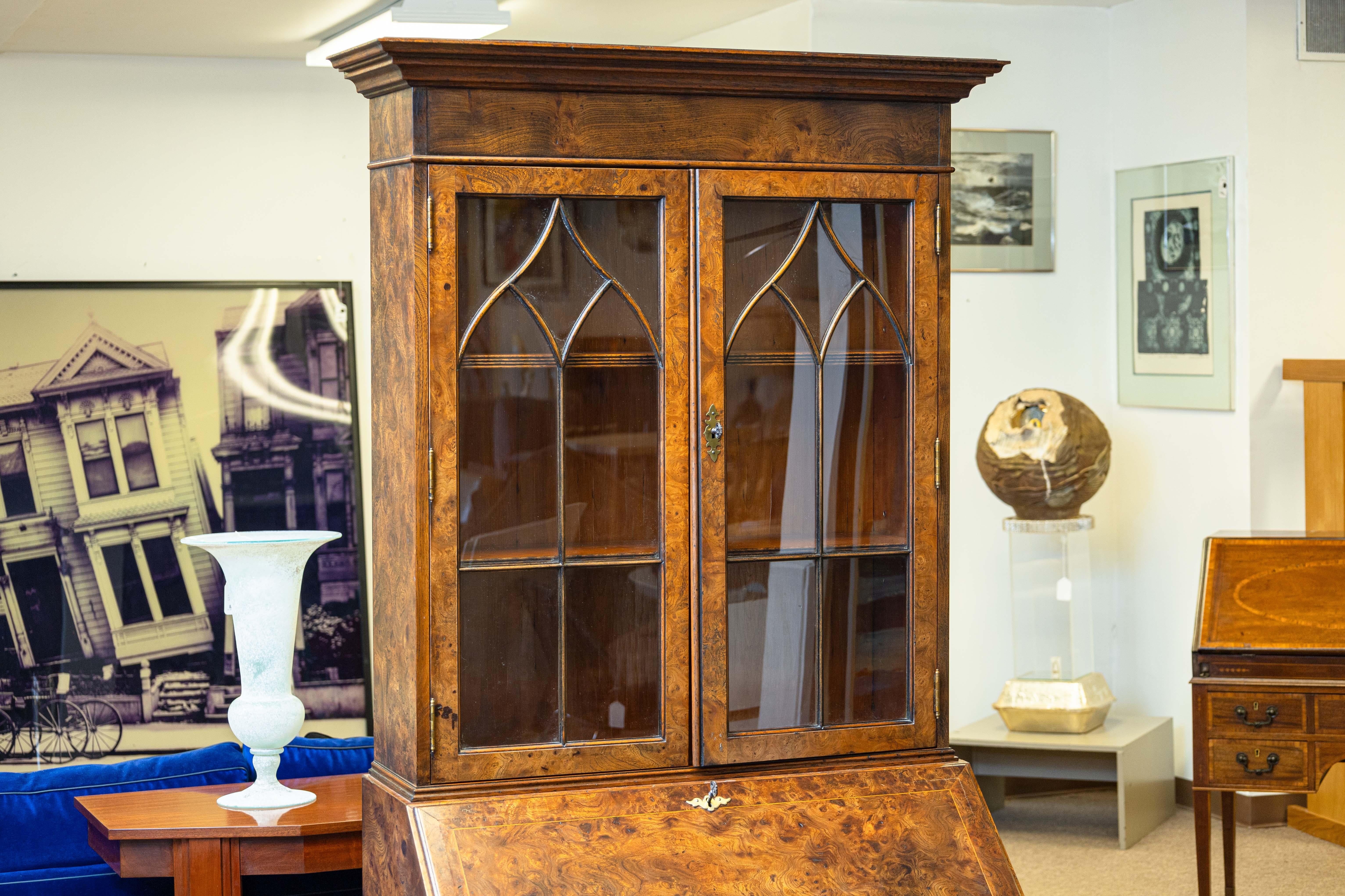 An antique Queen Anne style burr walnut bureau bookcase with secretary desk. Circa early 20th century. The top bookcase is behind glass doors to add an element of sophistication but also keep items protected. Front drop leaf secretary with many