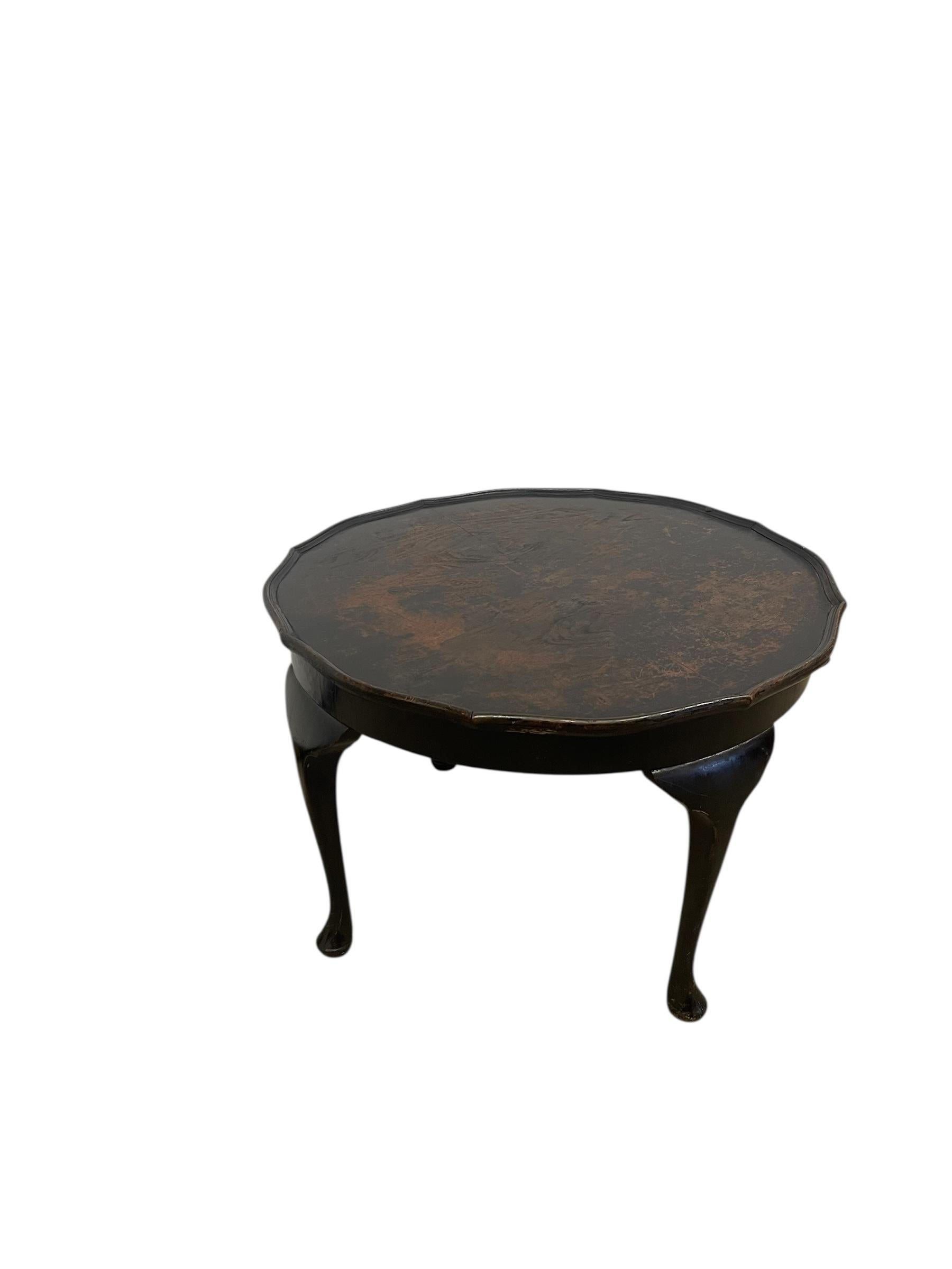  Questo probabile tavolino antico è realizzato in stile Queen Anne e presenta un piano rotondo con un bordo smerlato a galleria che si incurva sottilmente lungo il perimetro. Il piano è rifinito con una tinta scura e profonda con un caldo sottotono