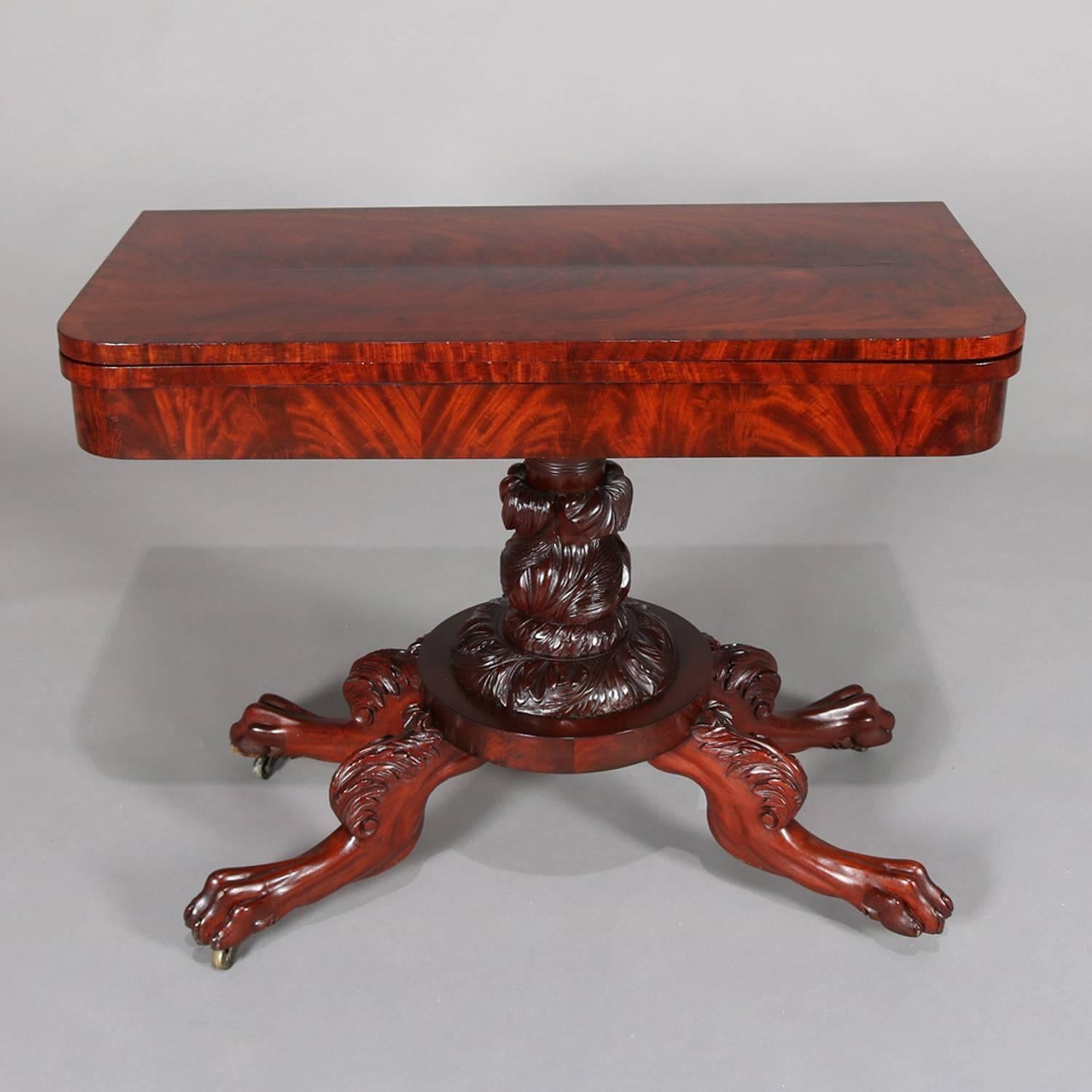Antique Quervelle School American Empire flame mahogany game table features deeply striated flame mahogany with hinged swivel game top above heavily carved Classical foliate plinth and raised on finely detailed lion legs terminating in claw feet and