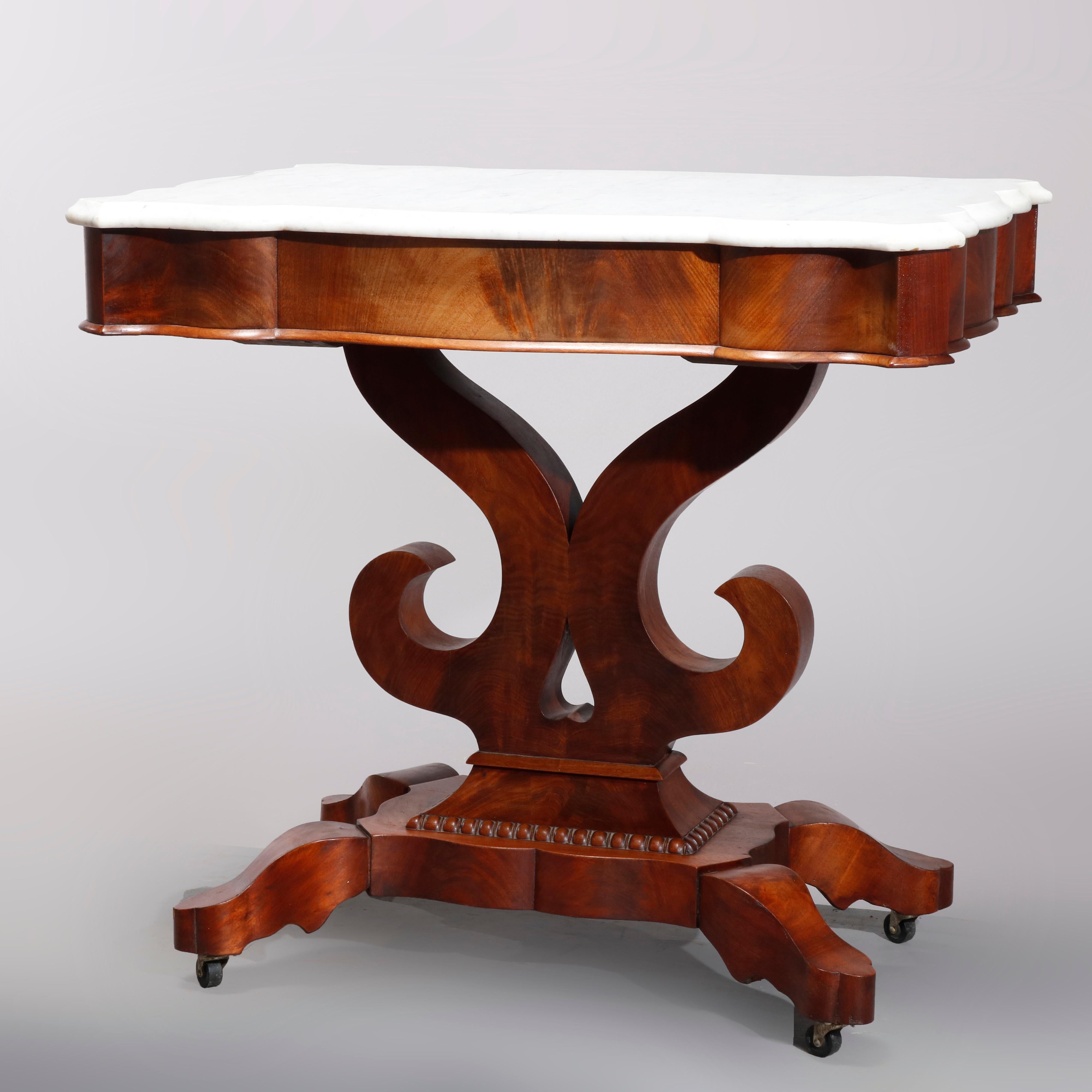 An antique American Empire turtle top center table in the manner of Quervelle offers shaped marble top surmounting flame mahogany base having deep skirt over scroll form plinth raised on four stylized cabriole legs with casters, circa