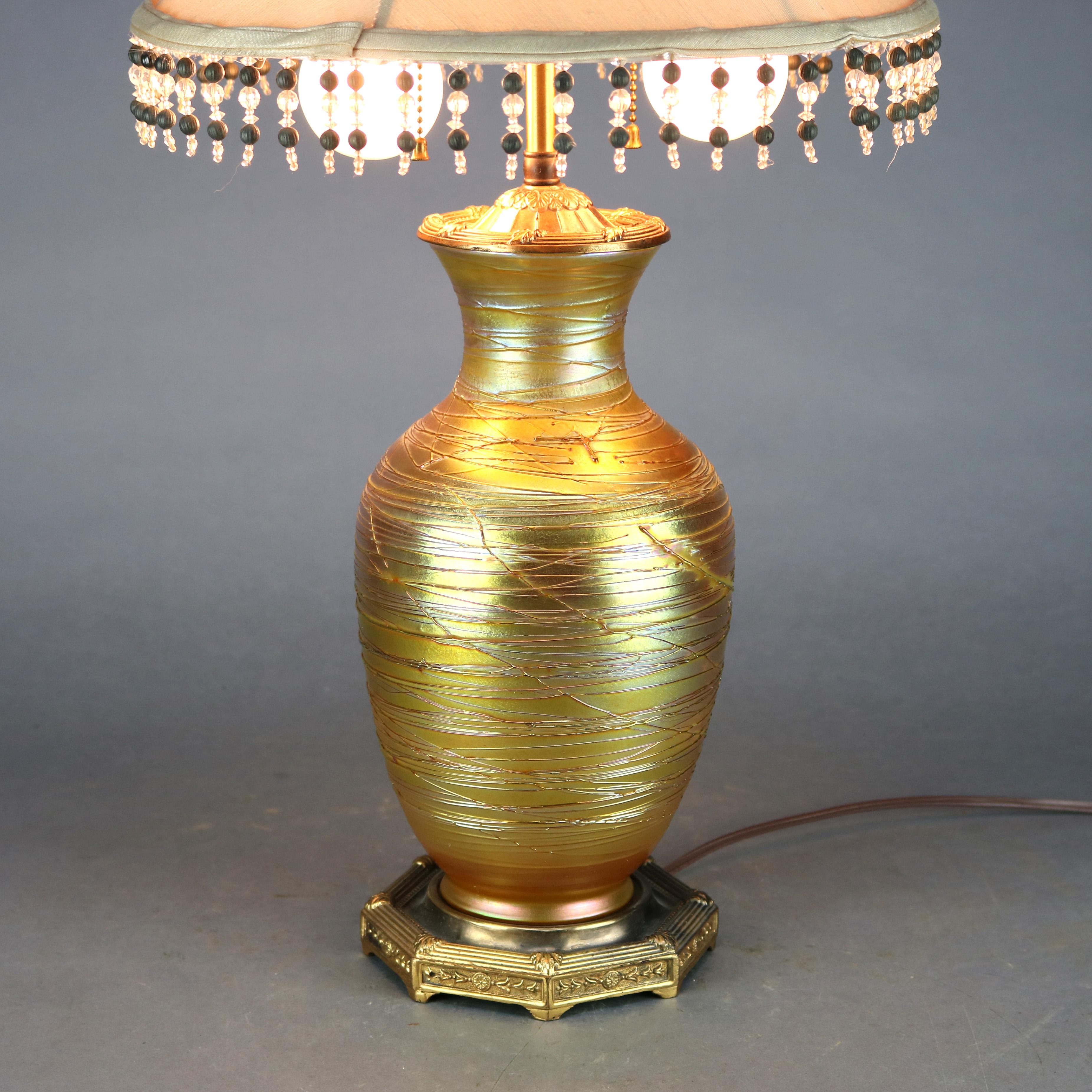 An antique double socket table lamp offers art glass string vase attributed to Durand with slip trail threading and gold aurene finish mounted on faceted cast brass base, also having elements of Quezal, circa 1920. This item was not disassembled to