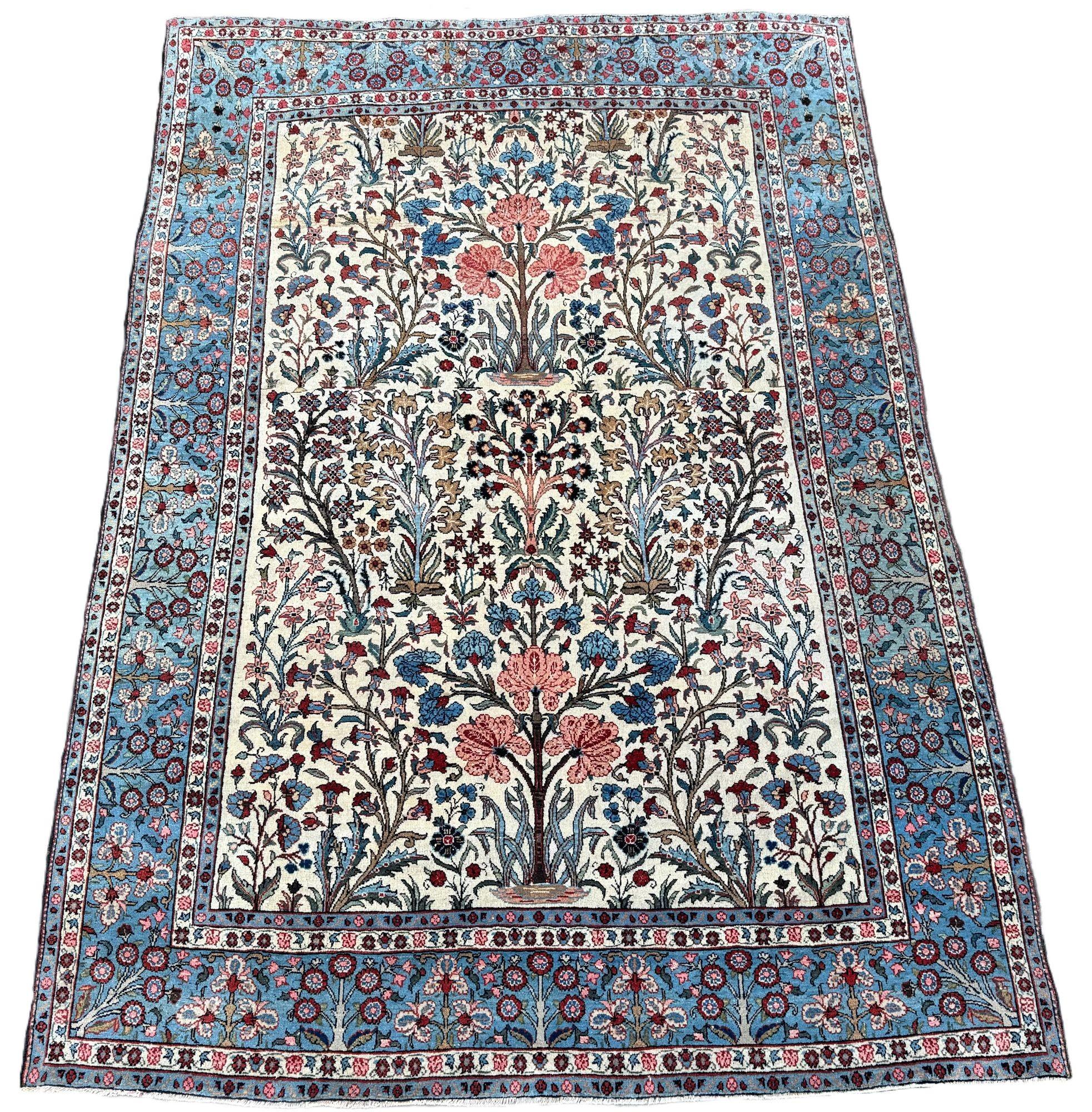 Ein wunderschöner antiker Teppich, gewebt in der Stadt Qum um 1920. Der Teppich zeigt ein stilisiertes Lebensbaummuster auf einem elfenbeinfarbenen Feld, das von einer ungewöhnlich hübschen, zartblauen Bordüre umgeben ist. Fein gewebt mit schönen