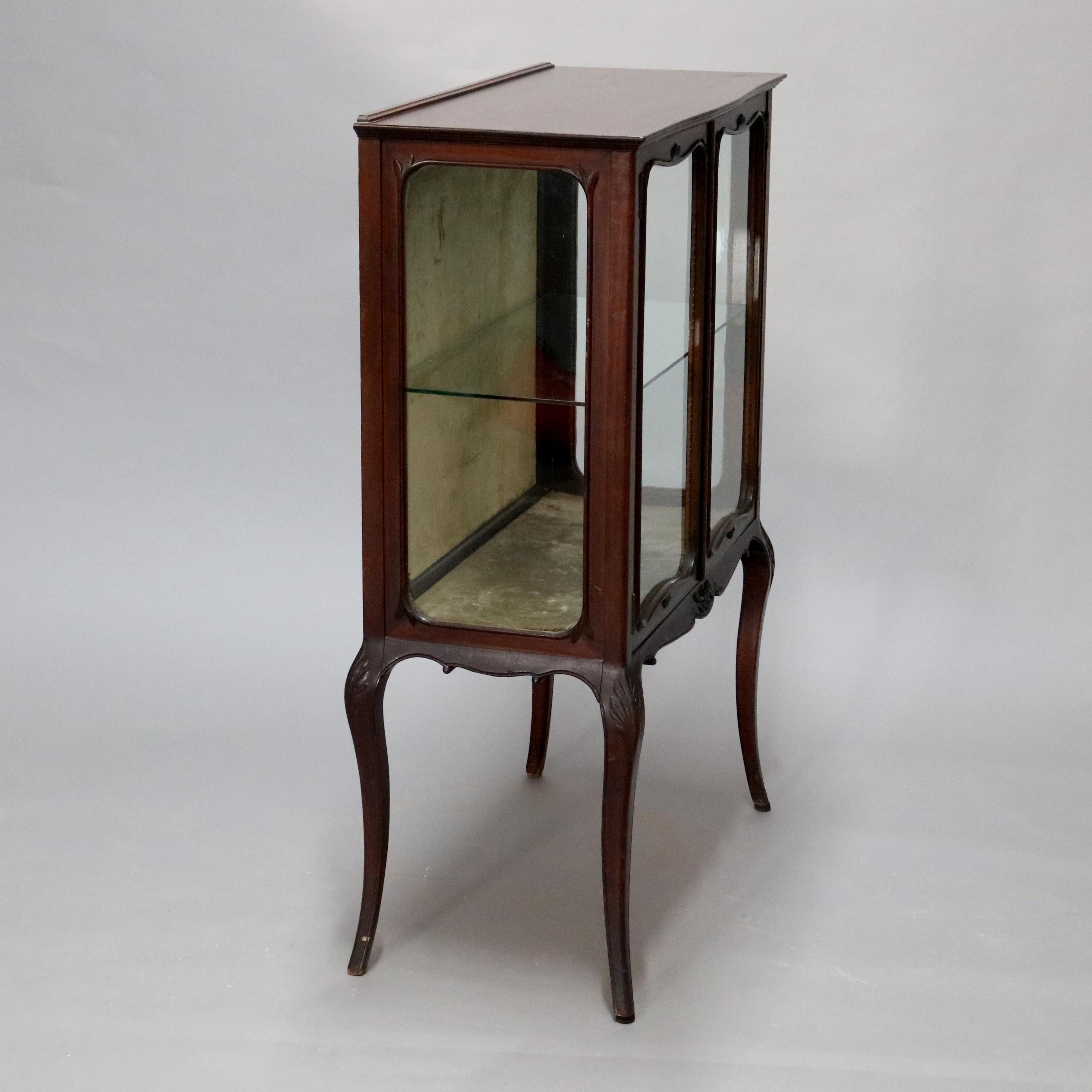 An antique R. J. Horner Louis XV style display virine offers mahogany frame with double doors having shaped windows, opening to shelved interior and surmounting base with carved skirt, raised on cabriole legs with acanthus carved knees, en vero