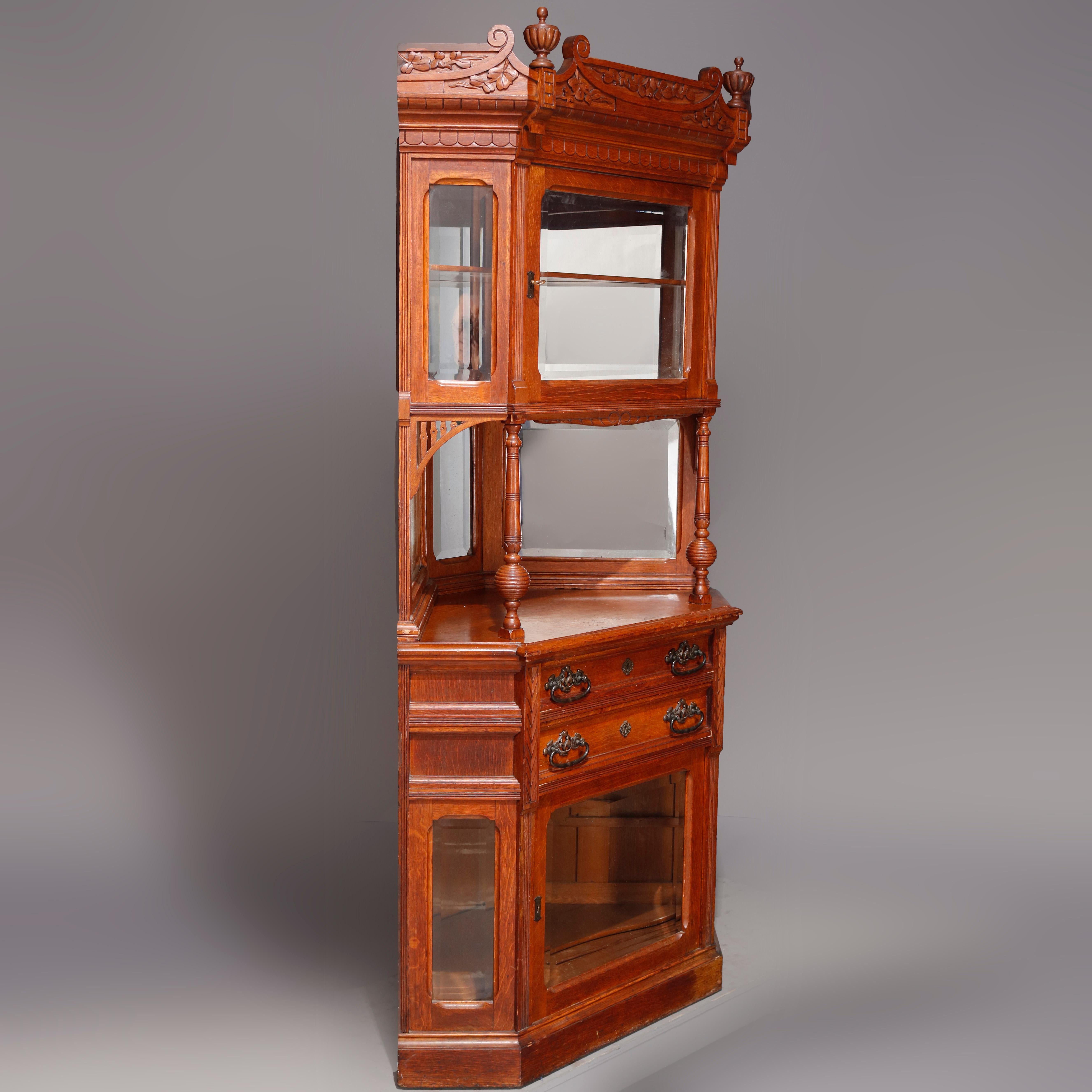 An antique R.J. Horner oak corner cabinet offers oak construction in aceted form with cared foliate and ur crest having flanking finials surmounting enclosed glass vitrine with mirror back and open gallery, lower case with two upper drawers over