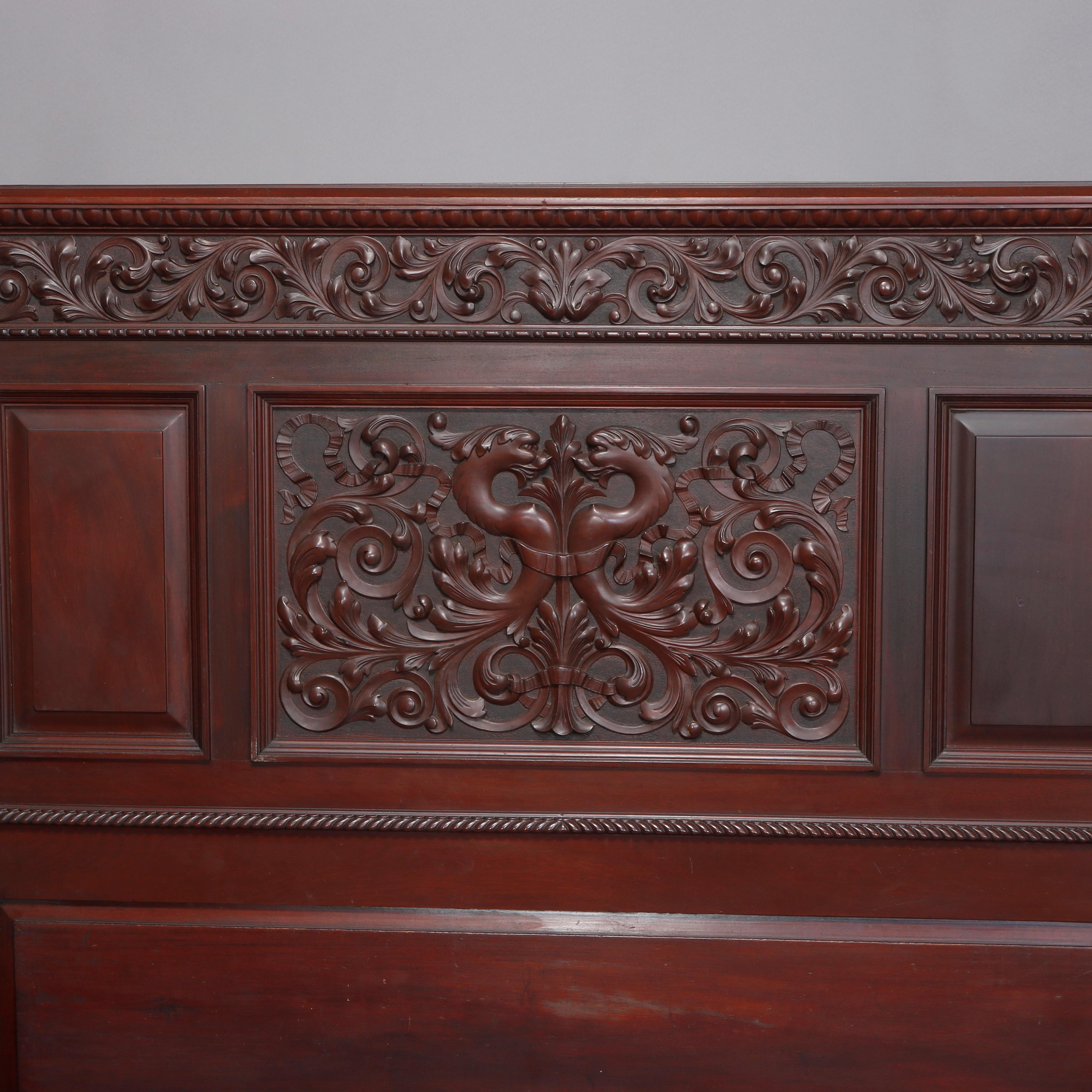An antique mahogany full/double bed frame attributed to R.J. Horner offers mahogany construction with paneled head board having intricately carved central facing griffins flanked on scroll, ribbon and foliate ground with flanking reeded columns and