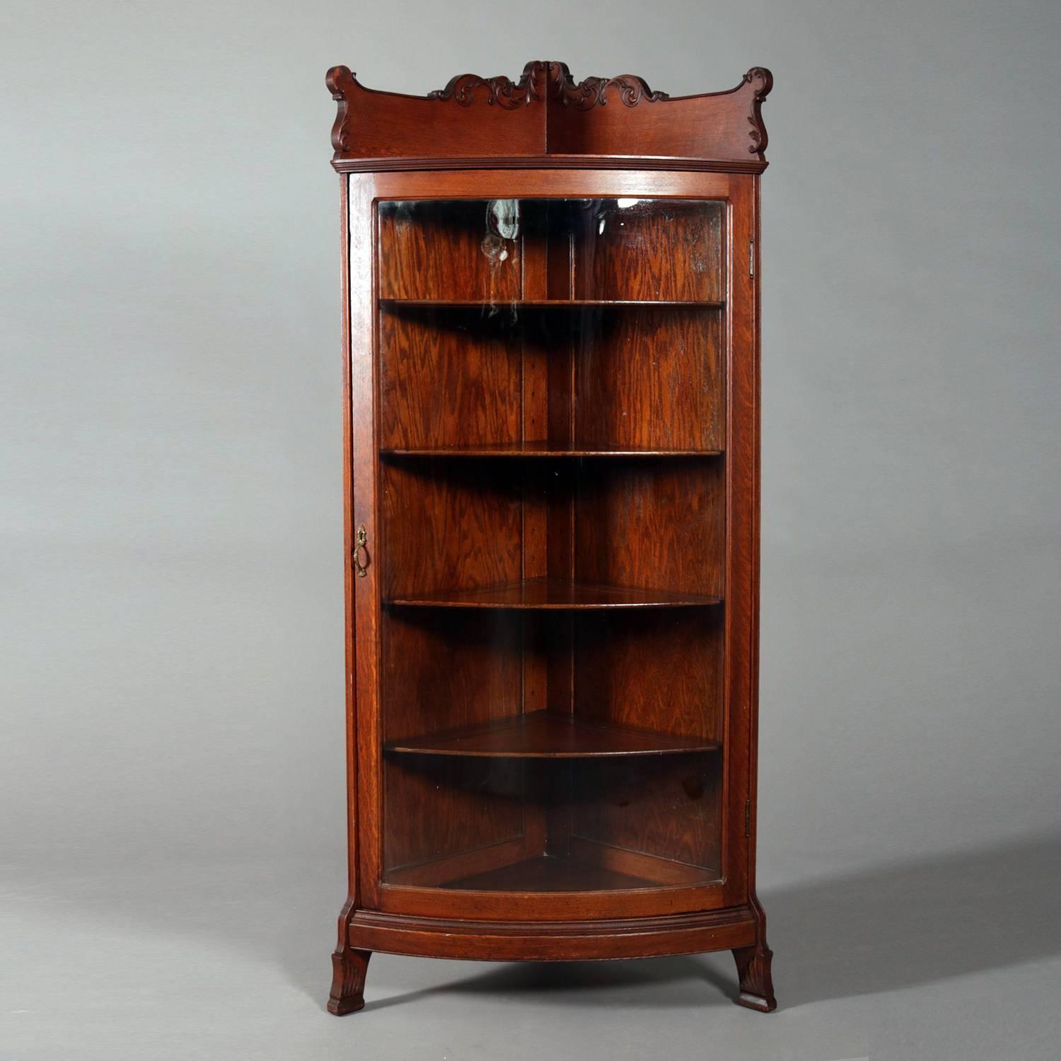 Antique R. J. Horner School cared oak corner china cabinet features rinceaux scroll and foliate backsplash, bow front glass door opening to adjustable shelf interior, circa 1910

Measures: 66