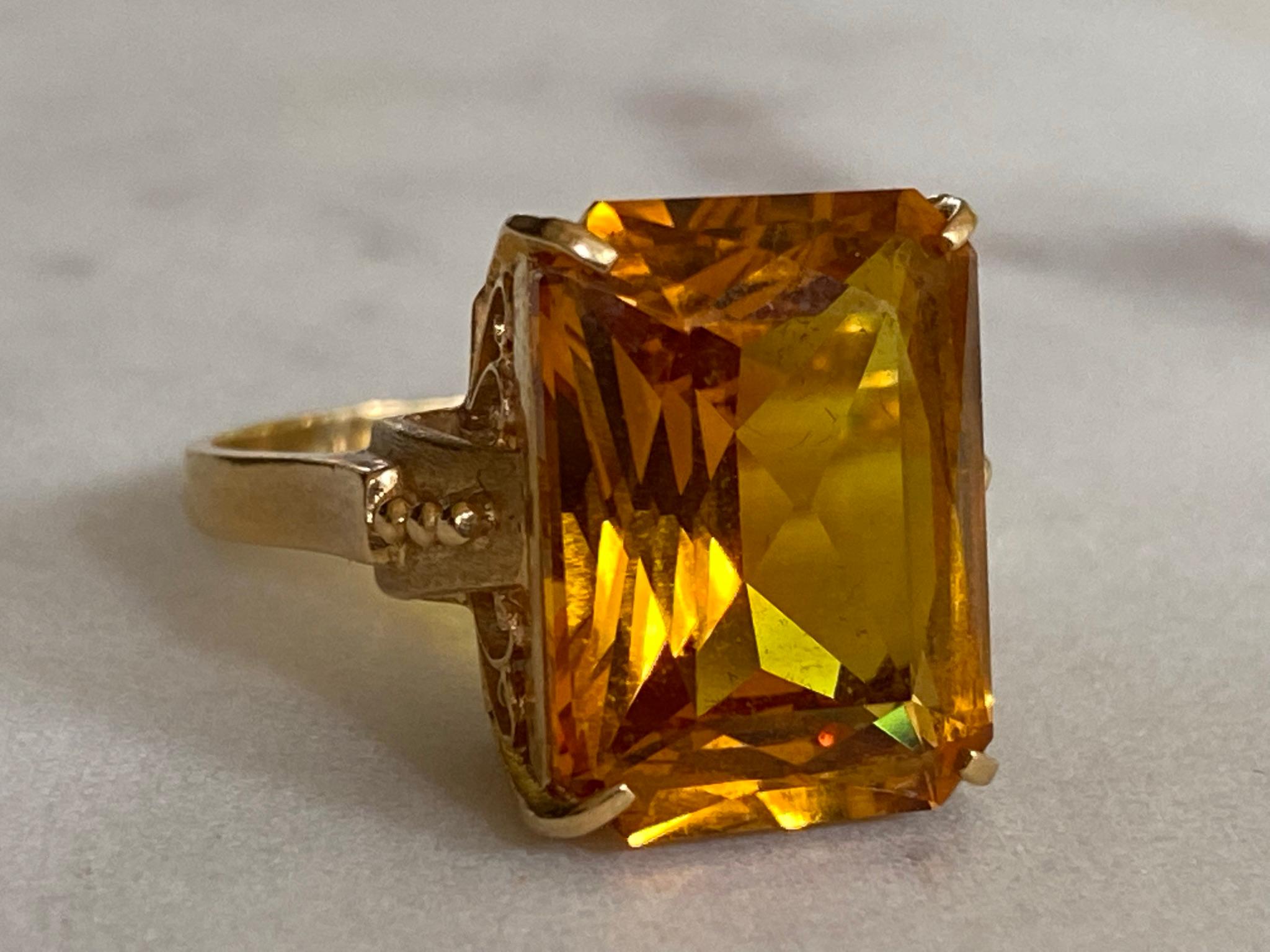 This antique cocktail ring features a large natural radiant-cut orange citrine measuring 12mm X 16mm set in an ornate, scrolling openwork gallery fashioned from 18kt yellow gold. Circa late 19th century with European stamps. 
