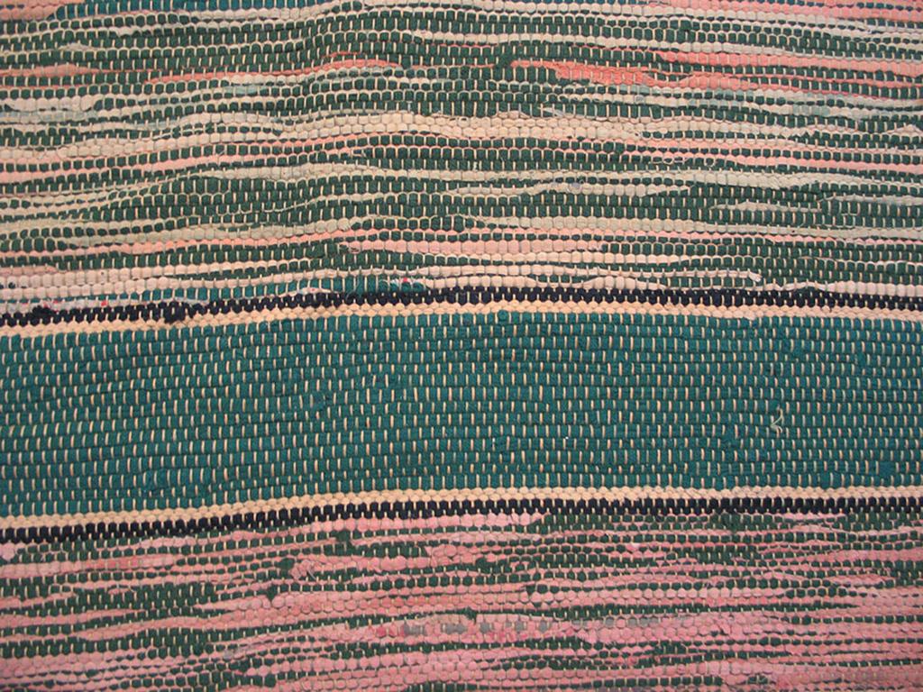 Dieser raumgroße Teppich von ca. 1960 hat ein gestreiftes Feld mit schlichten Bordüren an beiden Enden. Der allgemeine Farbton ist grün, aber es gibt auch viel Grau, Schwarz und Elfenbein. Dieser Flickenteppich wurde in einem Stück gewebt. Die