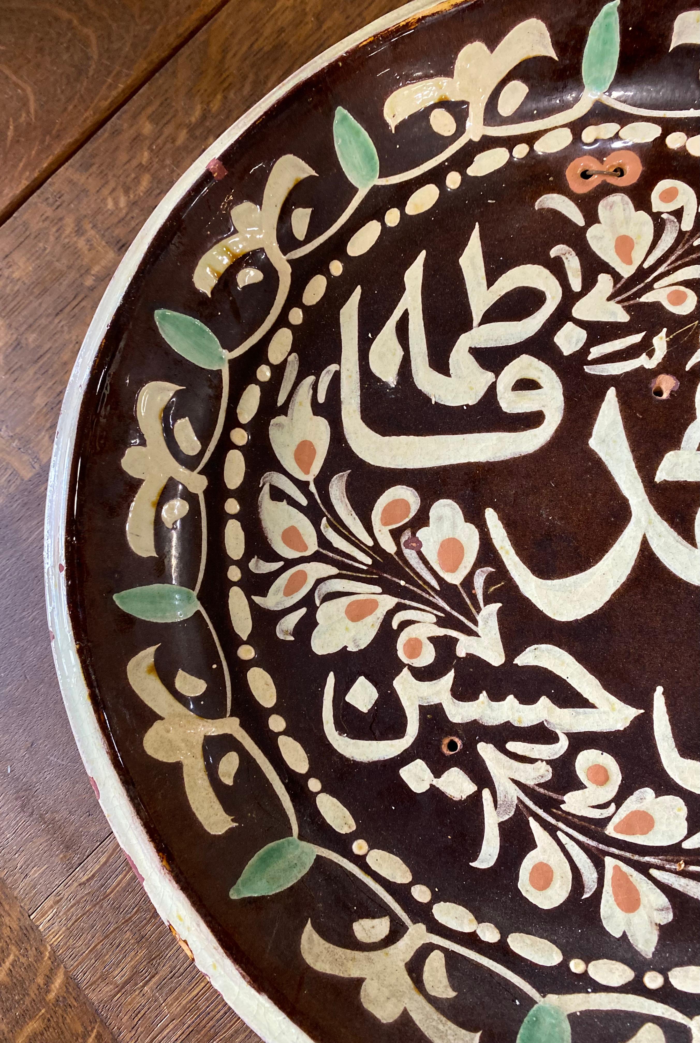 A stunning antique Arabic calligraphy round glazed terracotta wall plate having a lovely dark espresso background with warm white calligraphy and touches of mint green and peach. 

Arabic calligraphy is considered an art because it is a highly
