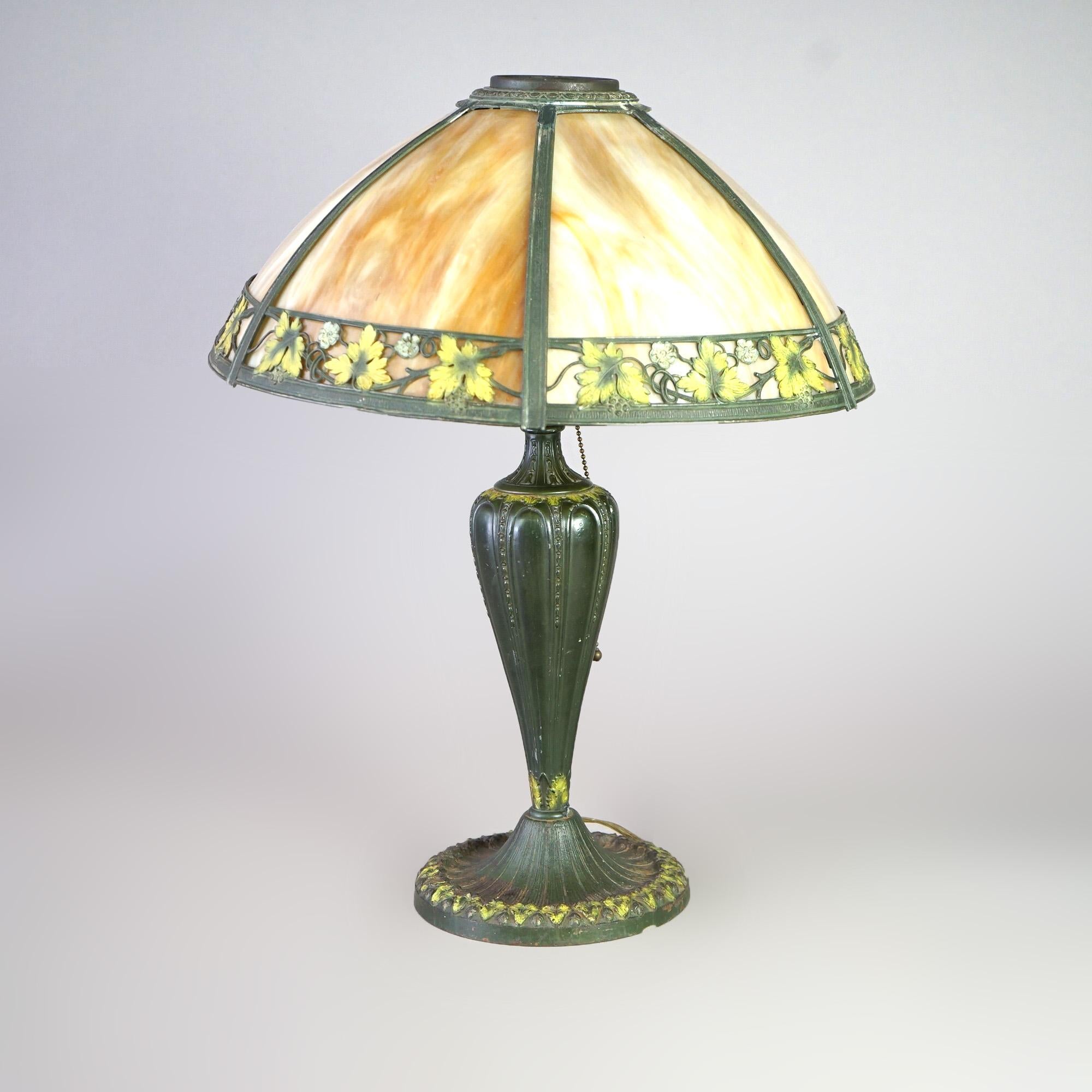 An antique Arts and Crafts table lamp by Raynaud offers polychromed cast single socket base with dome shade having polychromed leaf and berry design housing bent slag glass panels, c1920

Measures - 21