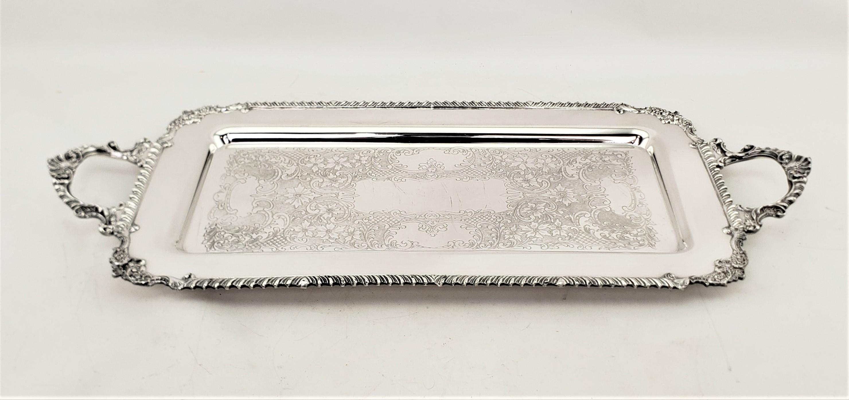 This narrowly constructed antique silver plated serving tray was made by the Old English Reproduction firm of England in approximately 1920 in a Victorian style. The tray is done with a stylized rope surround with accenting handles with scrollwork.