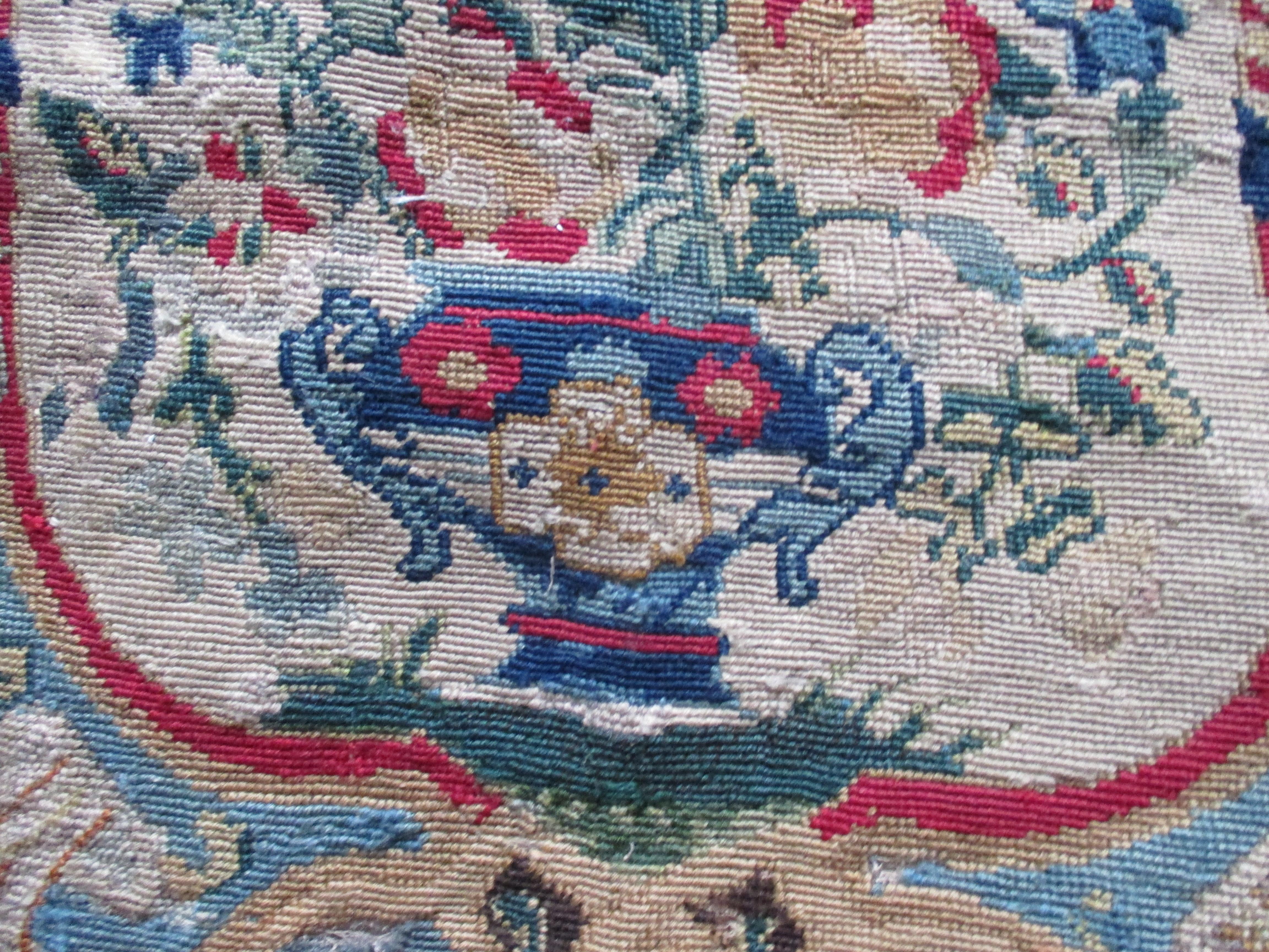 Antique red and blue floral petit point tapestry fragment with red medallion in the center.
With a red border and a bouquet of flowers on a blue vase in the center. 
 Ideal for re-upholstery or a decorative pillow.
In shades of blue, tan, red and
