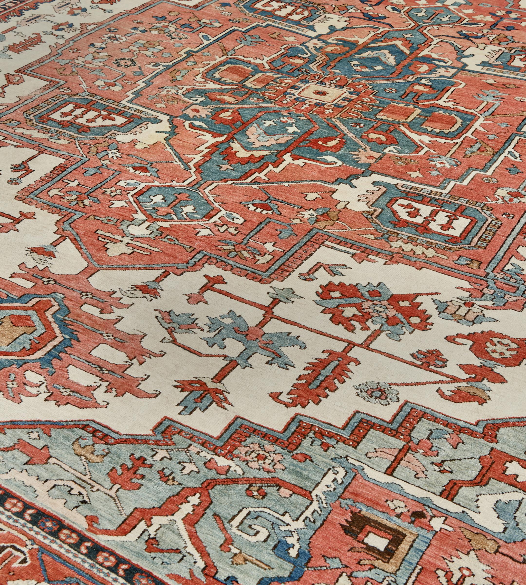 Questo antico tappeto persiano Serapi ha un campo avorio con palmette angolari rosso mattone, blu ghiaccio e blu medio e foglie seghettate e teste di fiori intorno a una losanga a gradini rosso terracotta con audaci pendenti di palmette, un