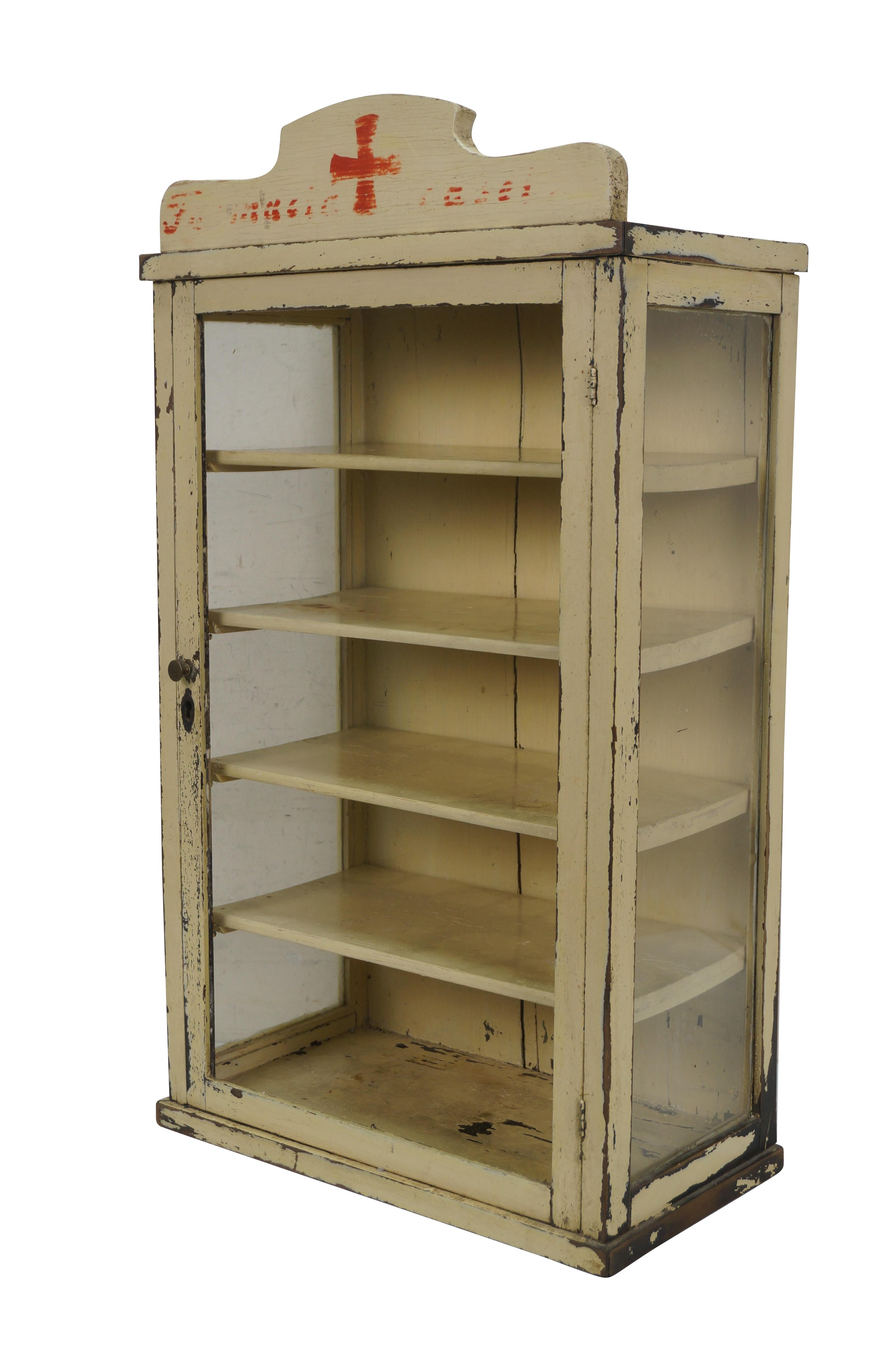 Circa early 20th century off white painted wall hanging medicine cabinet featuring five removable shelves and crest painted with a red cross and worn text.

Dimensions:

14.5