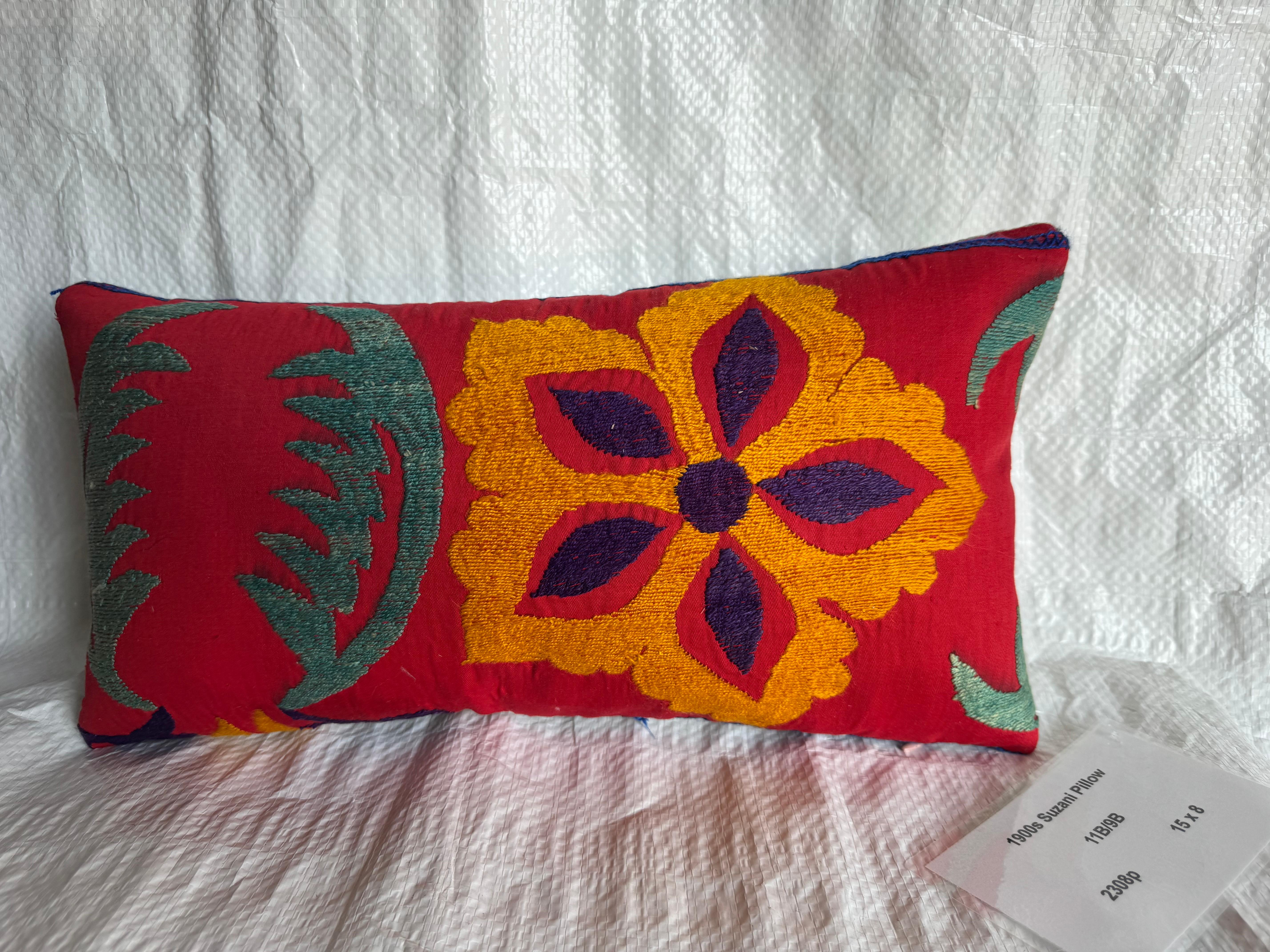 Vívido cojín suzani de principios del siglo XX bordado con atrevidos motivos florales en tonos amarillo dorado, ciruela y verde sobre una base de rojo intenso. El diseño refleja el arte tradicional del cosido a mano de Asia Central, donde se tejían