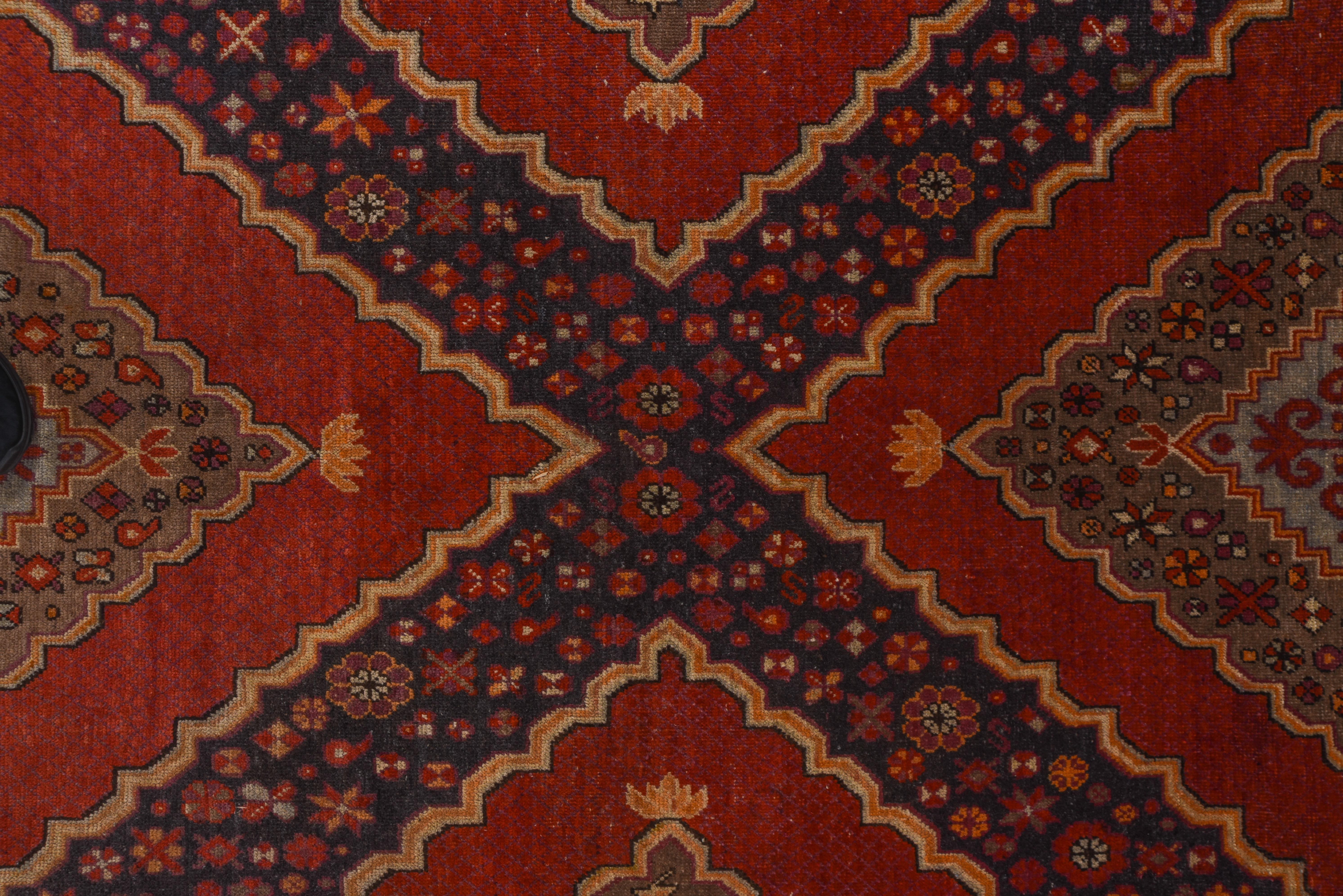 A double layered scalloped diamond pattern and en suite triangular side fillers in red, slate blue and celadon fills the field , and a teal border of double voluted lozenges frames the whole of this Xinjiang Province town carpet.