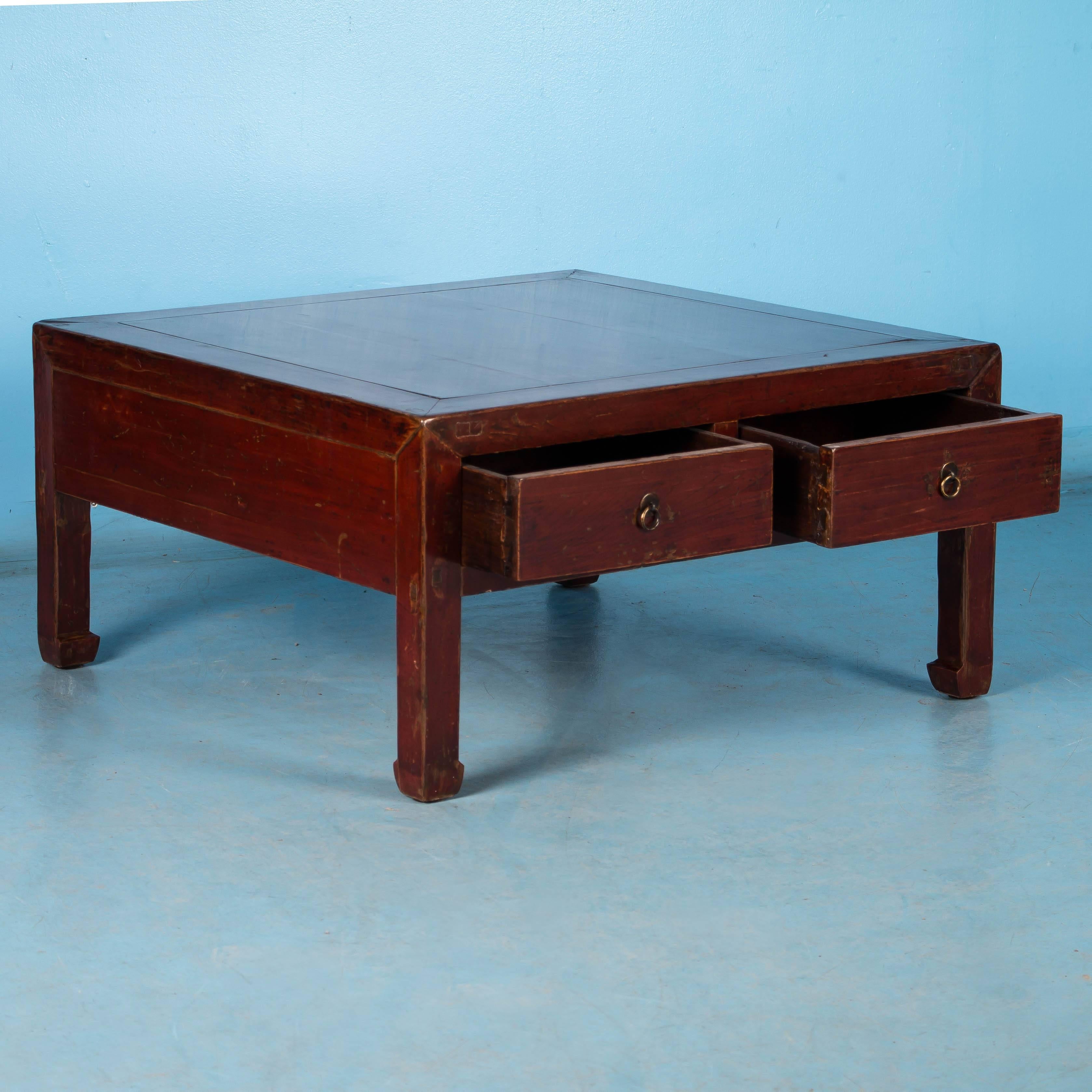 This square Chinese red lacquered coffee table, with it's simple, clean lines is made of elm and features a hard lacquer finish. The highly polished finish enhances the deep color which contrasts beautifully with the natural wood underneath where