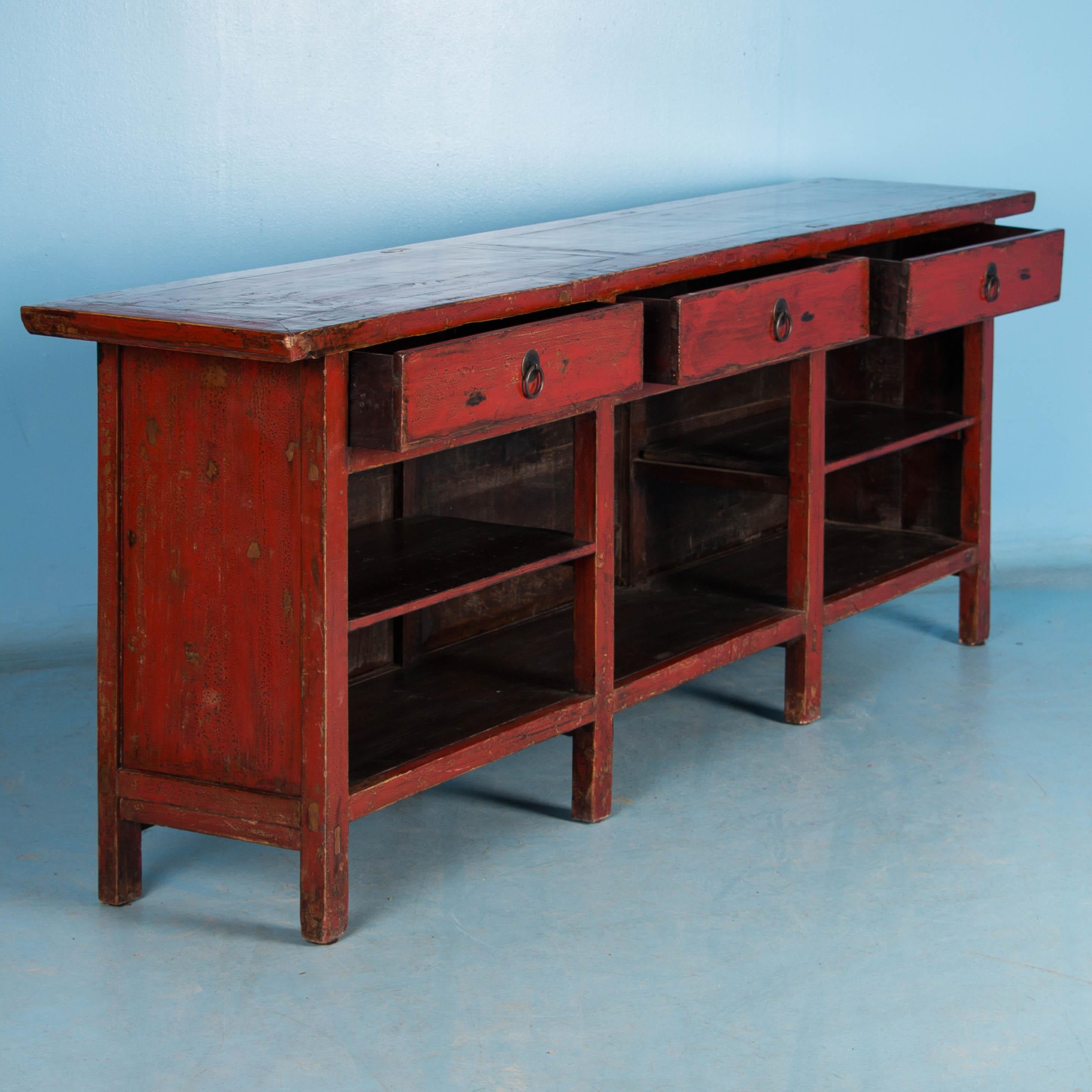 The highly polished lacquered finish gives this cabinet a sleek look and brings out the depth of the red paint. This long sideboard with three drawers and open shelving below is also painted inside the drawers and shelves and finished on all four