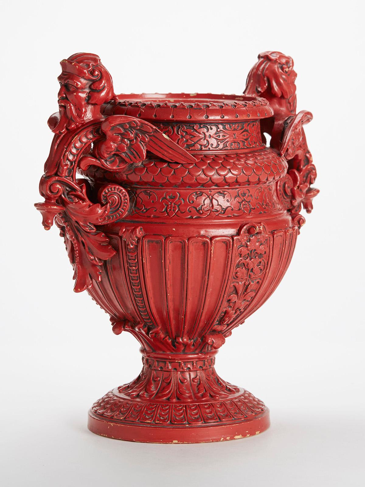 An impressive and large antique pedestal Majolica twin handled vase decorated in red glazes with relief moulded decoration and with winged god handles with moulded scroll and leaf designs. The heavily made earthenware vase stands on a rounded