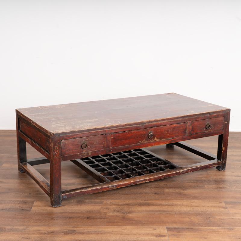 While entirely smooth, there is apparent texture to this coffee table due to the layers of red paint and natural wood that are revealed where the paint was worn off through generations of use. The polished lacquer protects and creates the finish