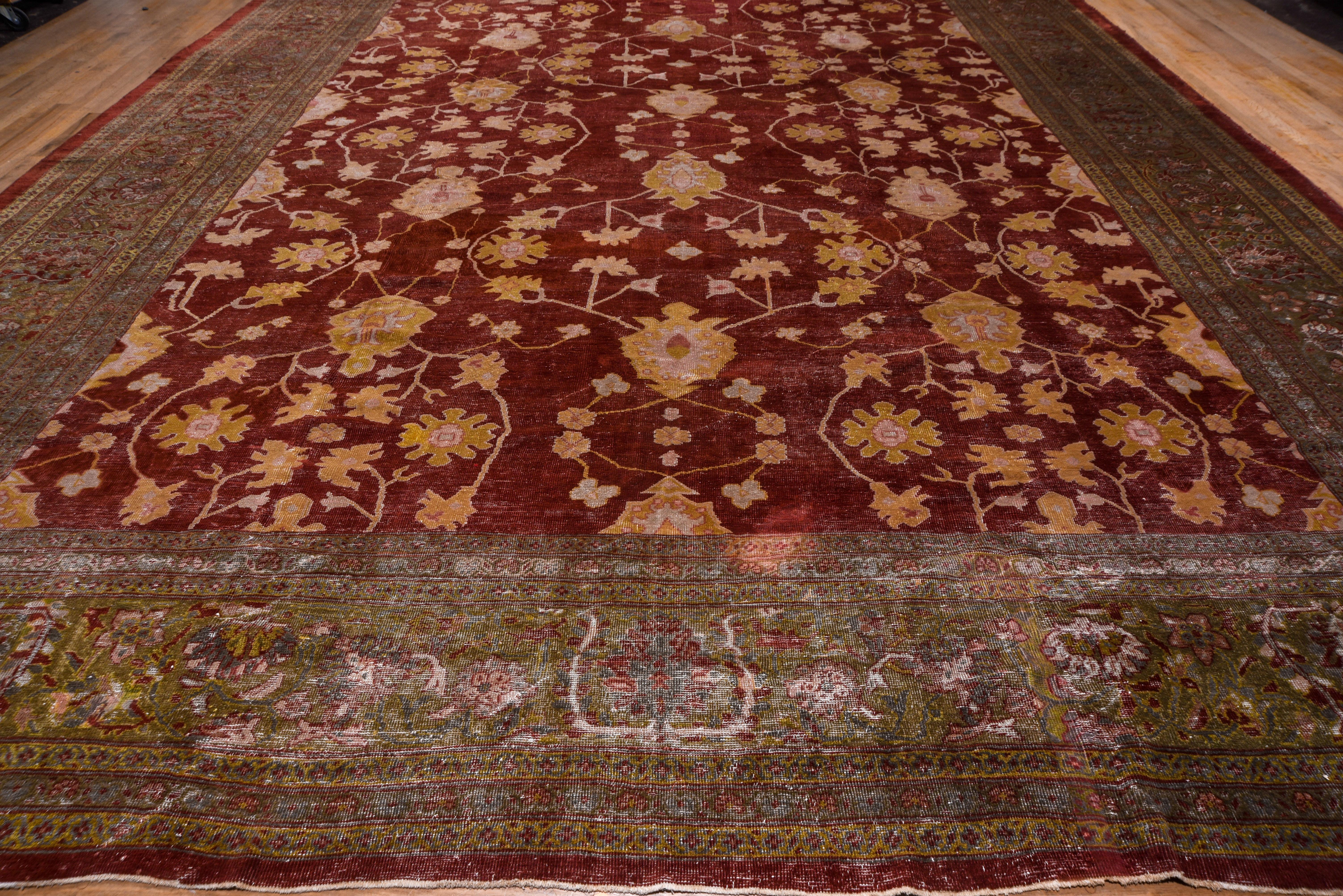 This very attractive, very large west Persian village carpet features a warm madder red field supporting a palmette, cogwheel rosette and curving stem design.