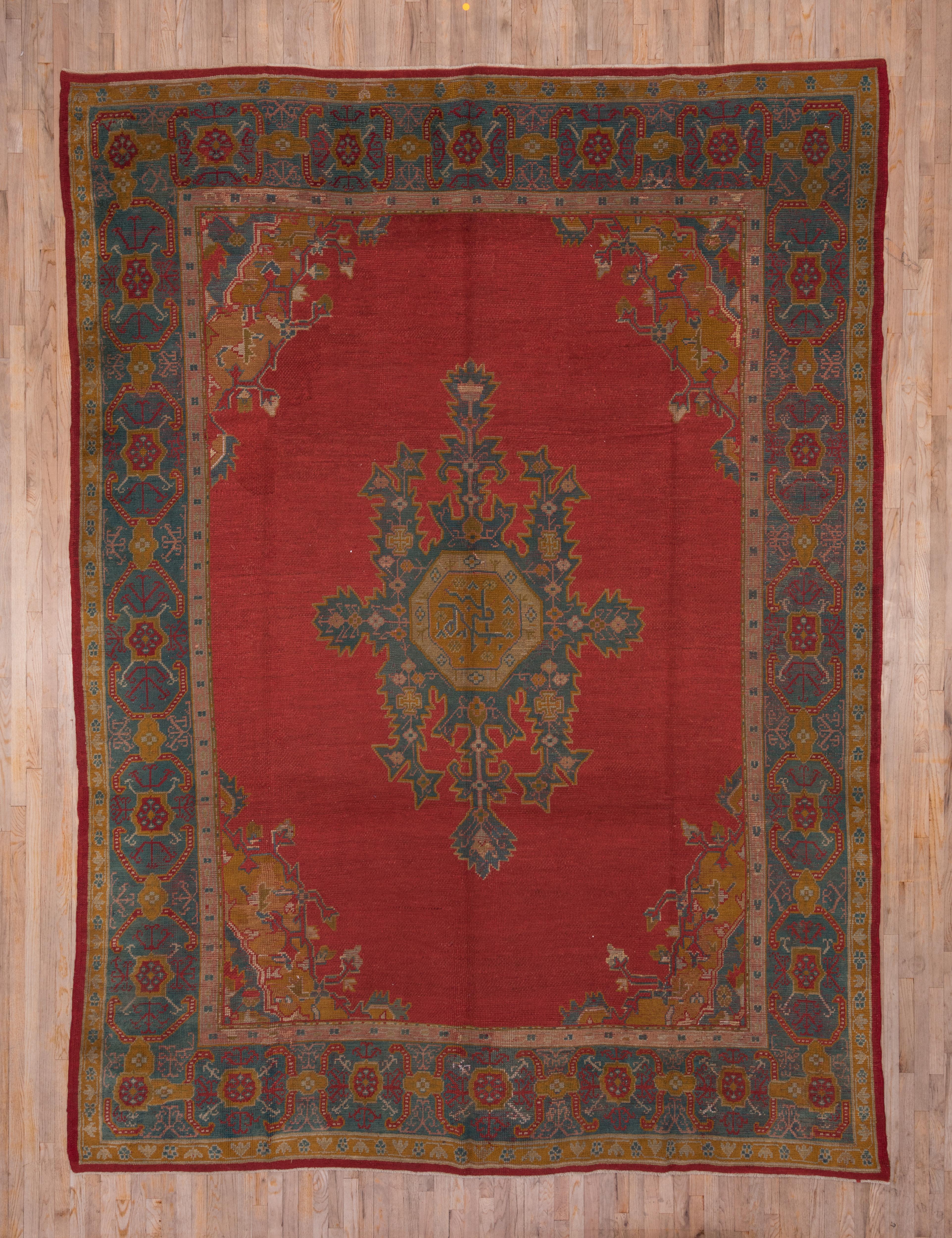 Das türkisrote Feld dieses Teppichs aus einer westanatolischen Werkstatt zeigt ein gezacktes, hängendes und gelapptes hellblaues Medaillon im allgemeinen persischen Heriz-Stil mit einem achteckigen Zentrum und Goldruten-Ecken, aus denen kleine