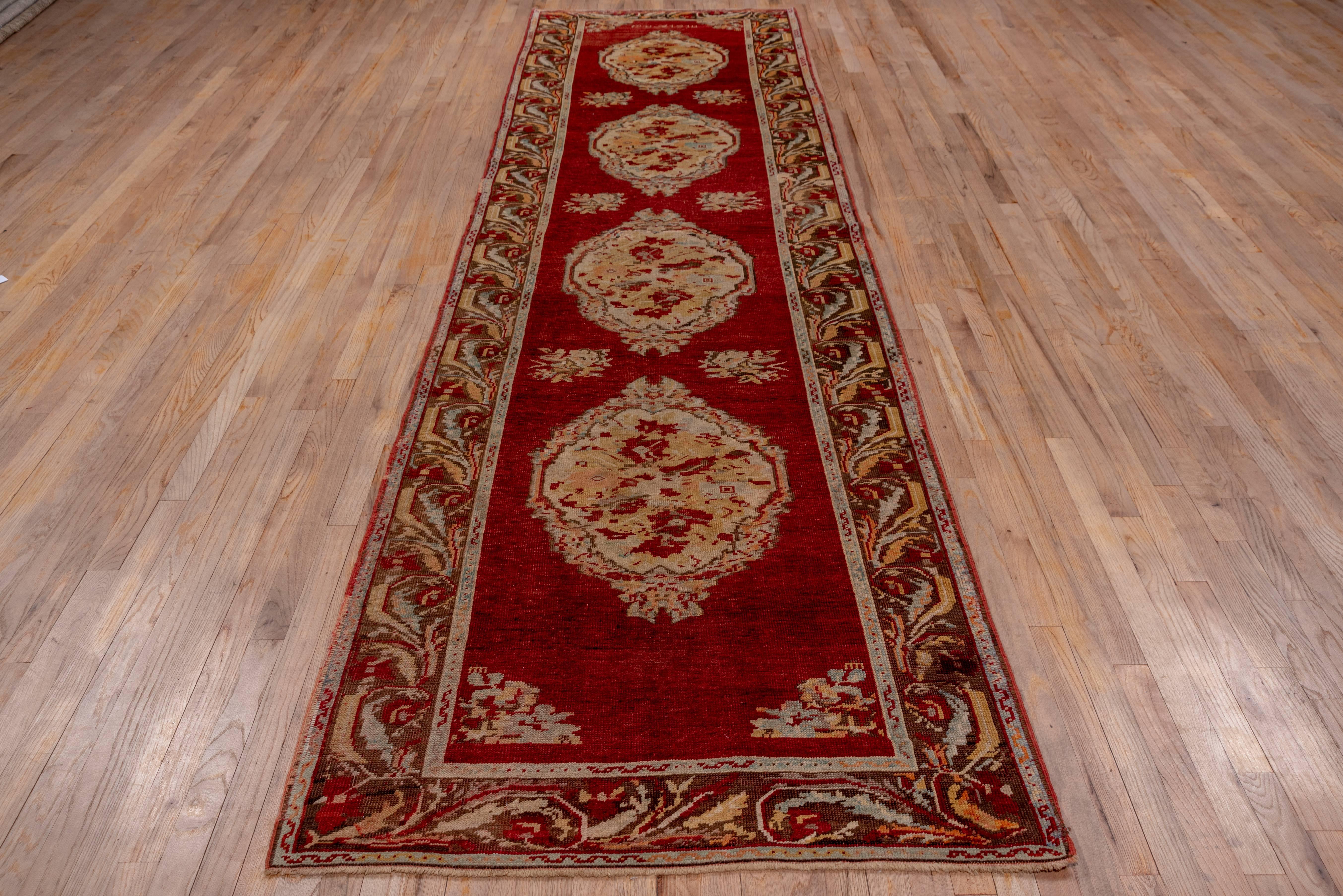 Four oval medallions in French floral style decorate the red field of this western Turkish runner. Small rose bunches fill in along the sdies of the field. A semi-realistic acanthus leaf border frames the whole. The style is reminiscent of Karabaghs