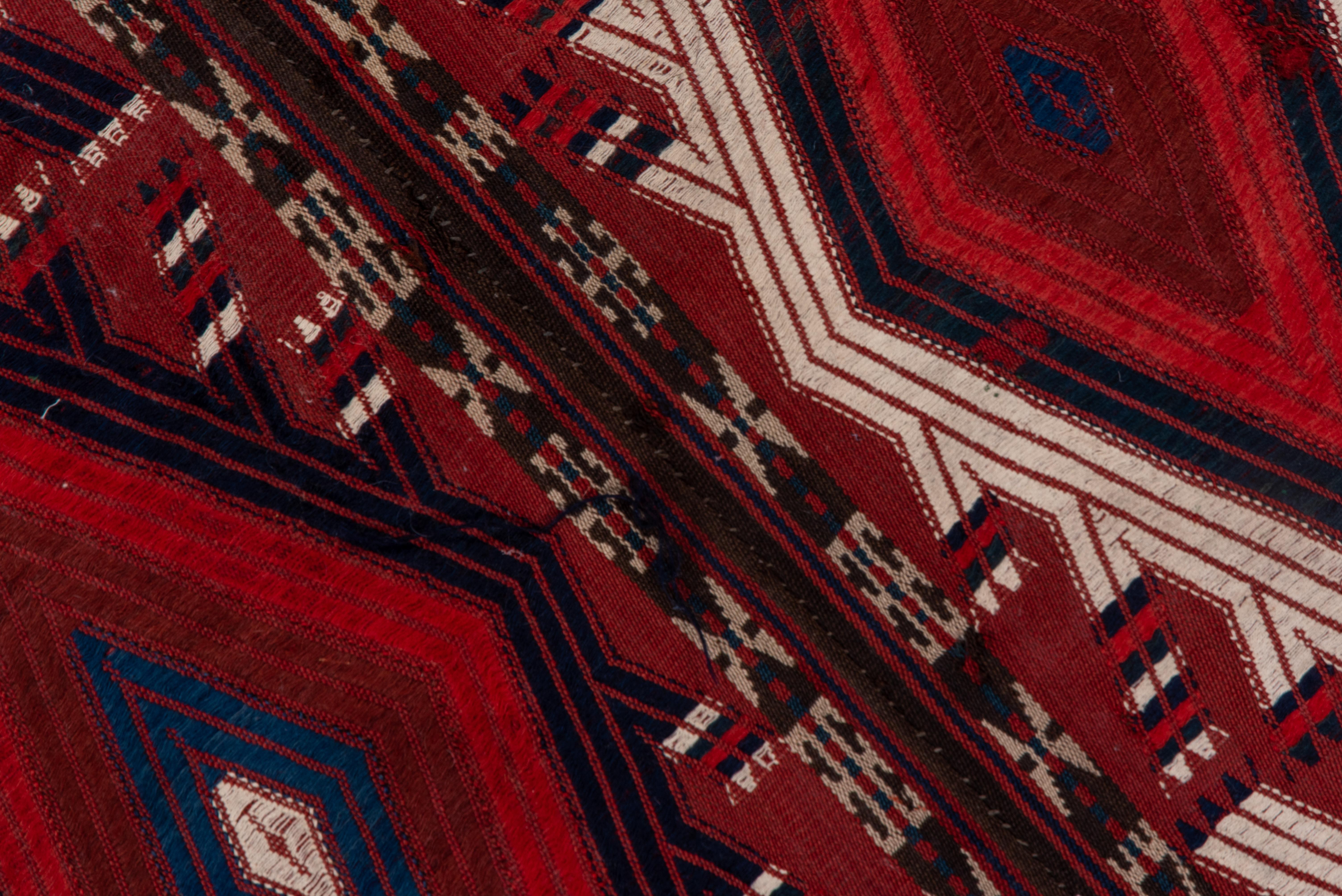 Composed of four strips edge joined of a Yomud tent band, this Central Asian nomadic textile artifact shows a repeating tall lozenge design with rams' Horn finials. White cotton highlights a palette in two reds and two blues.