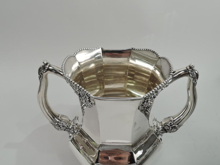 Turn-of-the-century Edwardian sterling silver trophy cup. Made by Reed & Barton in Taunton, Mass. Faceted baluster with scalloped and beaded rim. Reeded and leaf-capped, -wrapped, and -mounted side handles. Four leaf-mounted open scroll supports.