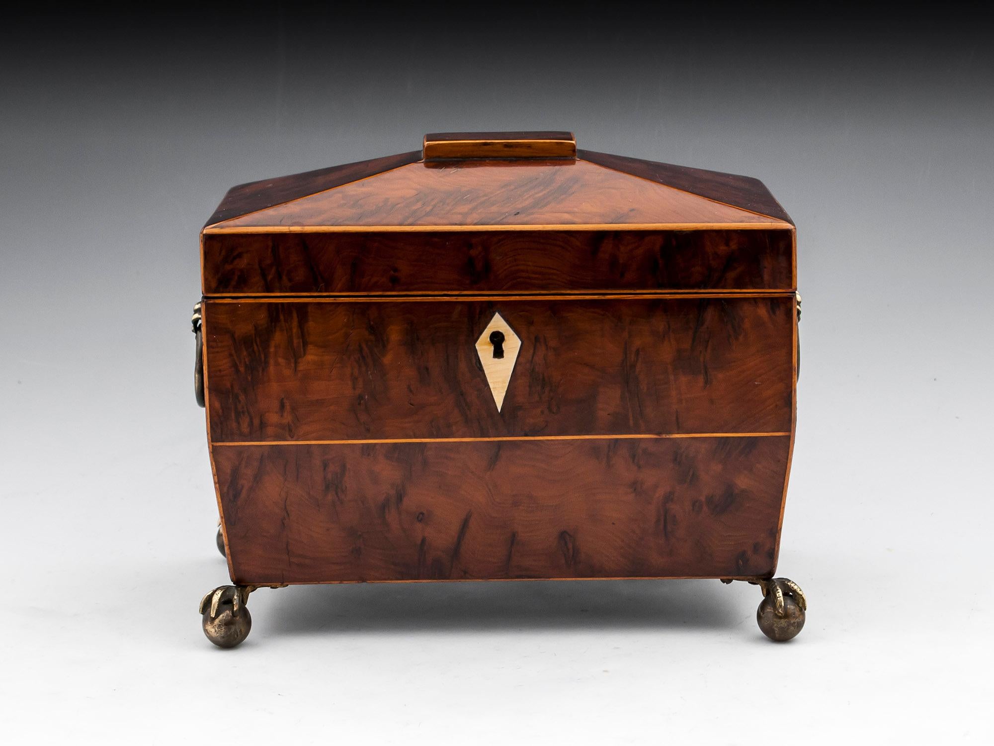 A small, twin burr yew tea caddy by H. Spencer. Edged in boxwood, with lion mask side-handles and brass ball and claw feet. The underside of the lid is lined with red leather on which is the rare feature of the maker’s label reading: H. Spencer,