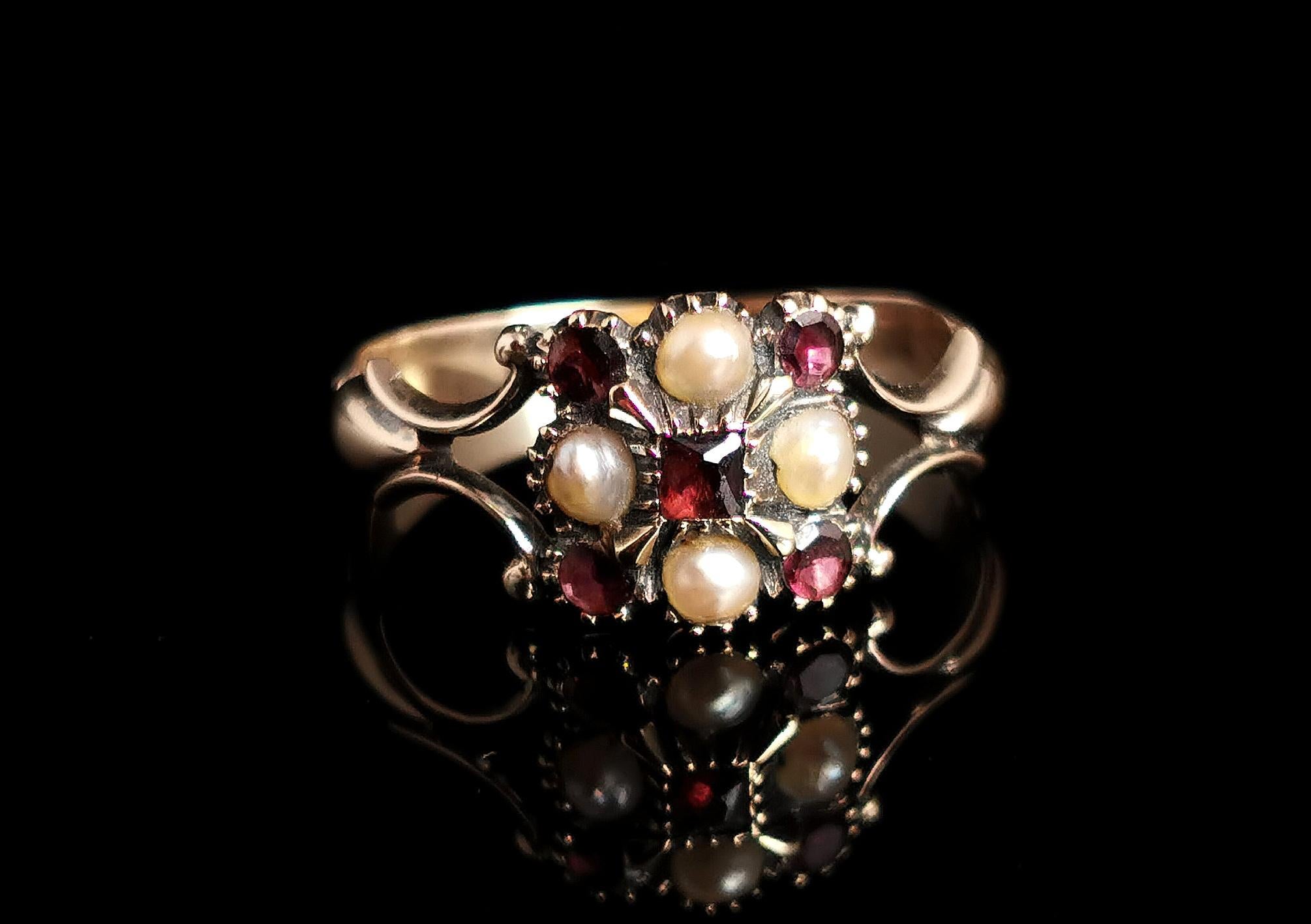 A beautiful antique Regency era ring.

This pretty piece features a central floral arrangement of garnet and seed pearl, set out in an almost chequer board design, the stones set in sterling silver.

The ring has decorative split shoulders with an