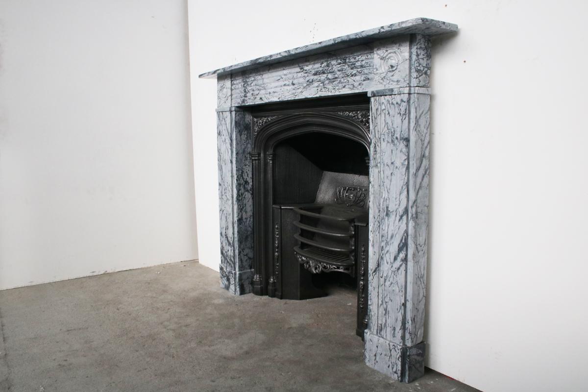 Regency bullseye fireplace surrounds in Bardiglio Fiorito marble with fluted frieze terminating in roundel carved capitals above similarly fluted jambs. Circa 1830.

Pictured with an original cast iron grate, priced separately.