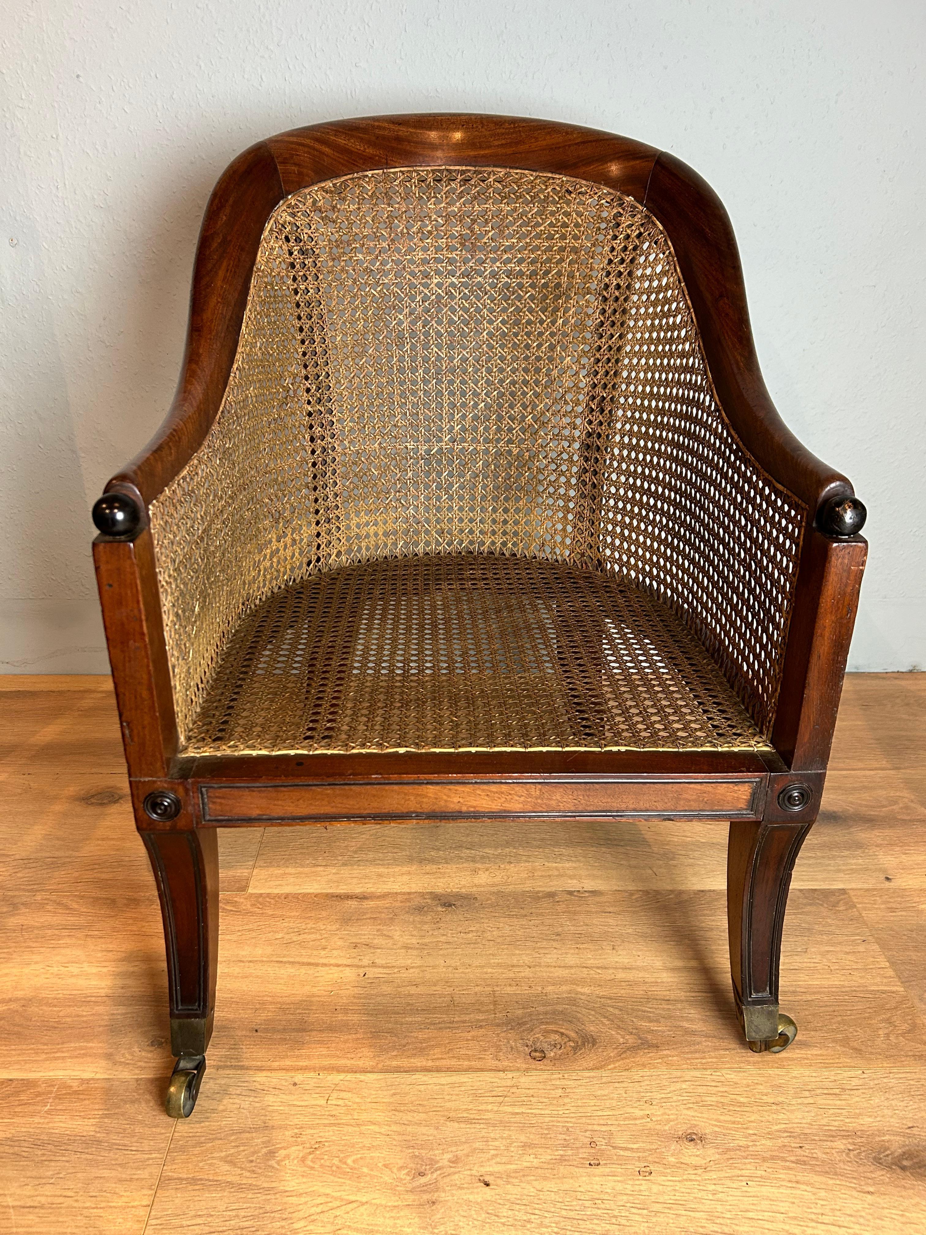 English mahogany bergere arm chair Regency period circa 1815 attributed to Gillows. Frame caned throughout with arched top rail and down swept arms ending with ball ebonised terminals on moulded sabre legs with applied turned roundals to the front