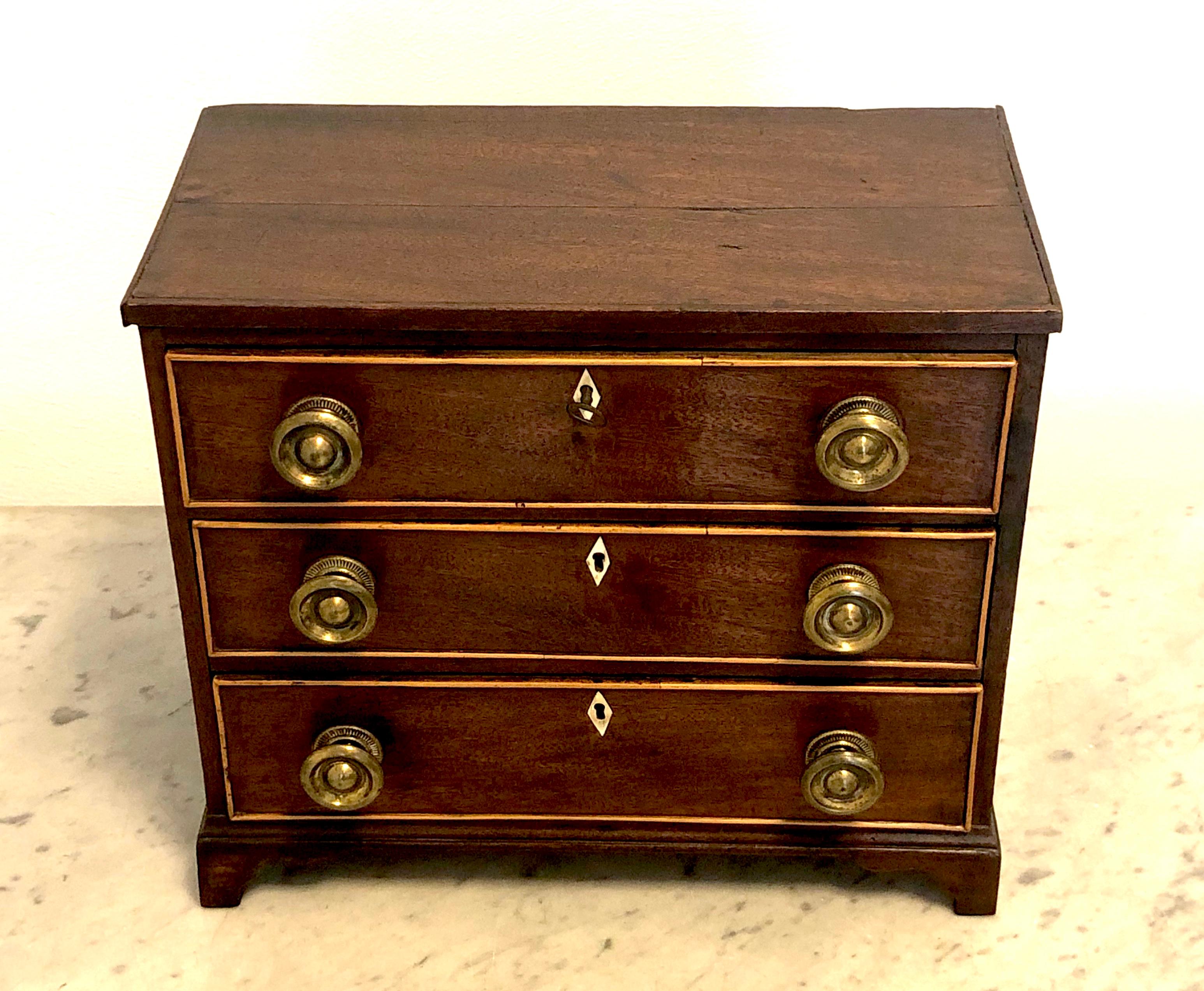 This charming miniature chest of drawers is made out of mahogany with boxwood bandings around the three drawers. It features bone keyhole decorations, original mounts, locks and a key,
England, Regency, circa 1815-1820.
 