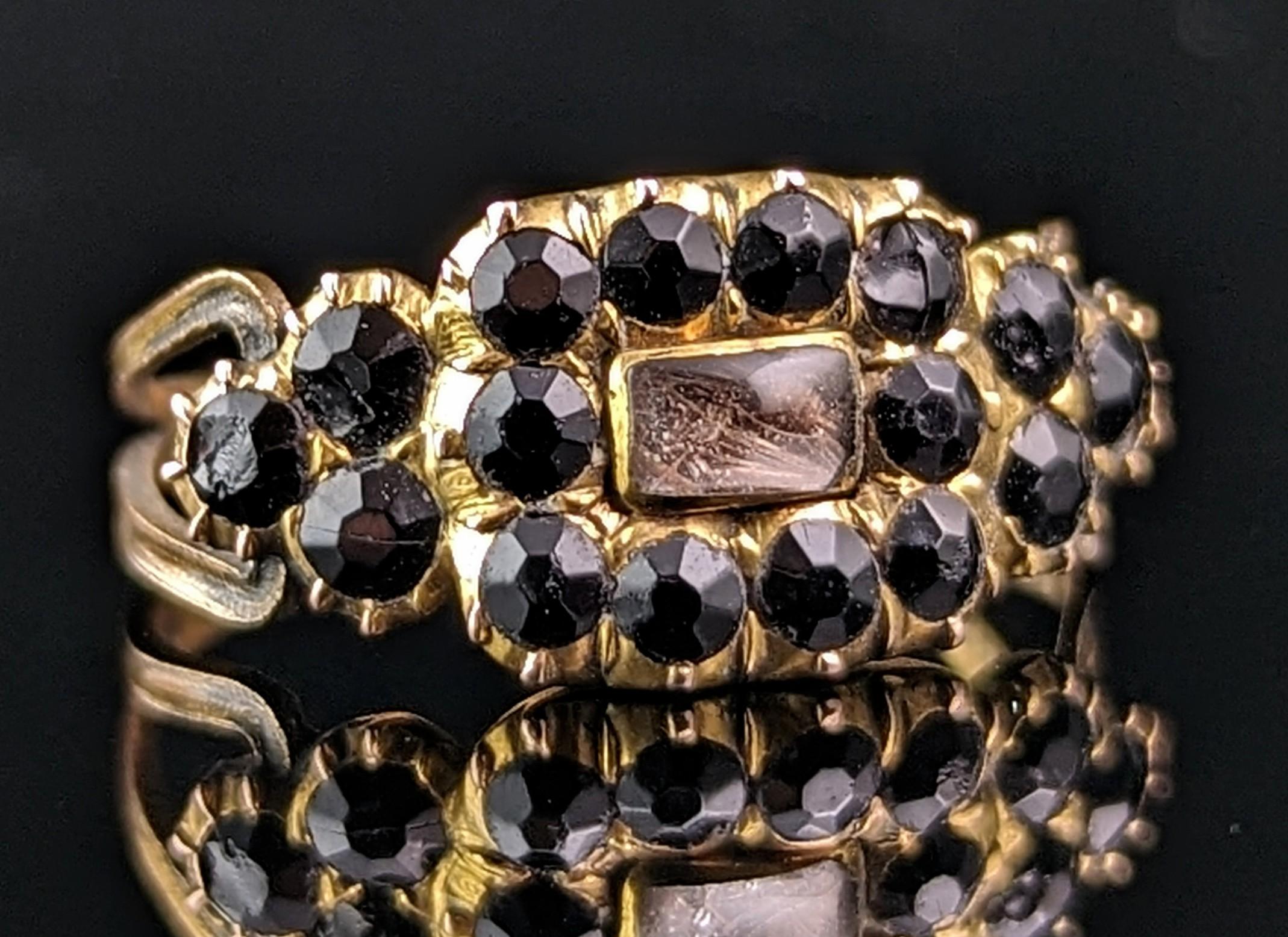 A bittersweet and beautiful Regency era mourning ring.

The ring has a rounded rectangular face with a domed crystal panel enclosing hair beneath the panel.

Surrounding this is a halo of Vauxhall glass stones in rich inky black that lead down to