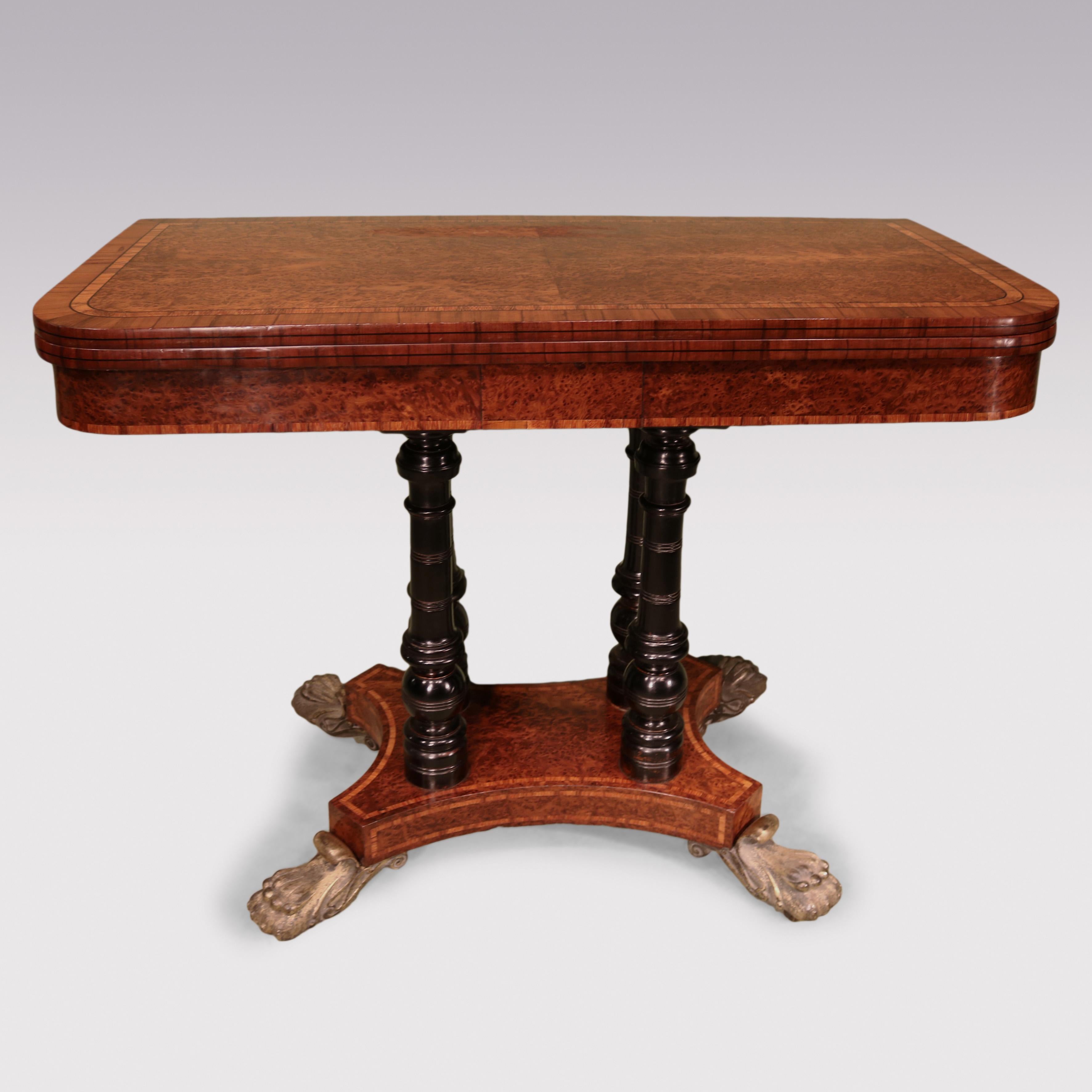 A late Regency period burr yew wood card table with quarter veneered rounded rectangular fold over top with baise lining.  The table raised on turned ebonised baluster supports with  concave base and canted corners, ending on bold brass scrolled