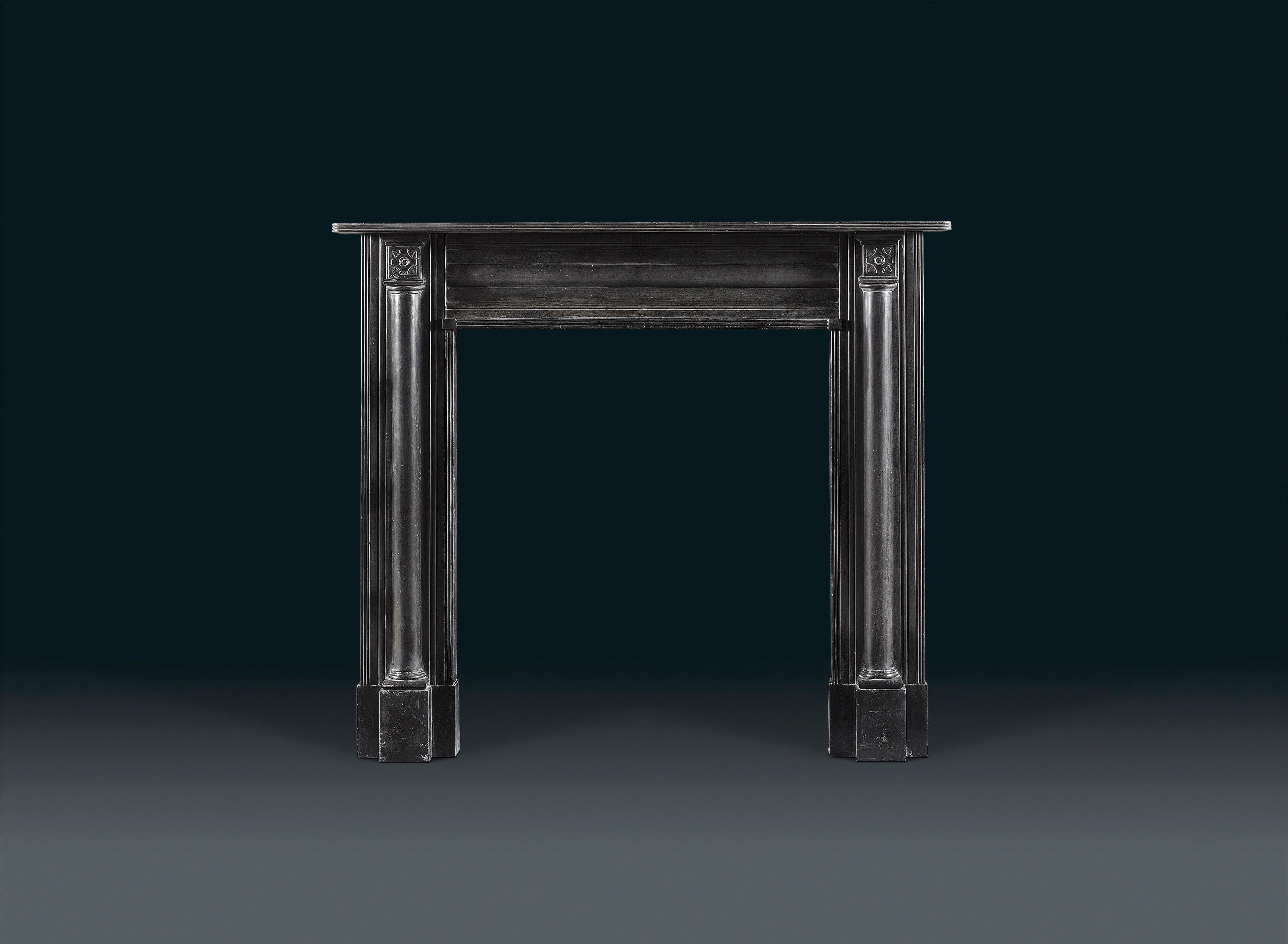 A Regency Belgium black marble chimneypiece is of restrained neoclassical form. The simple, reeded shelf sits above projecting end blocks carved with a stellar motif, and supported on either side by architectural half columns on the jambs. The