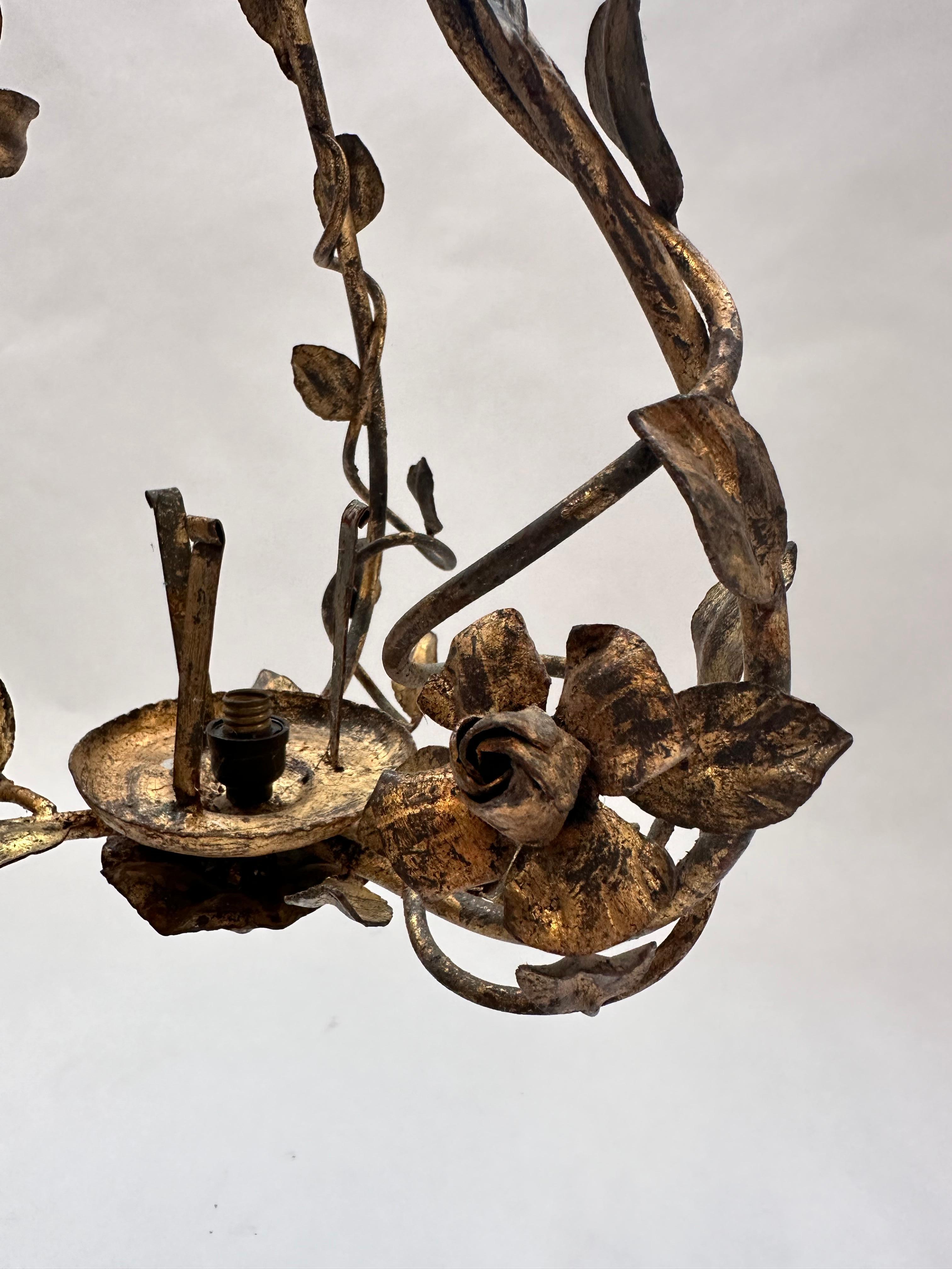 Il s'agit d'une suspension en fer forgé avec un motif floral et de vigne. Le luminaire présente un design ornemental forgé à la main, avec des vignes en métal torsadé et des feuilles et des fleurs délicatement travaillées. La finition semble être un
